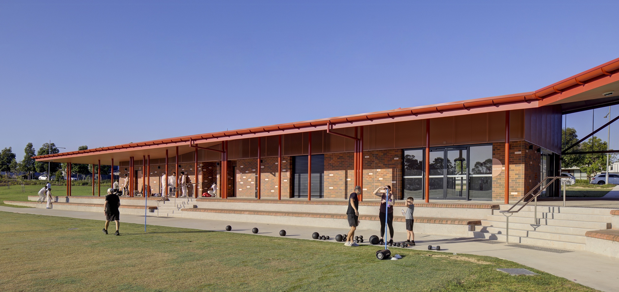Covered veranda with slender steel columns and tiered concrete seating overlooking the playing field