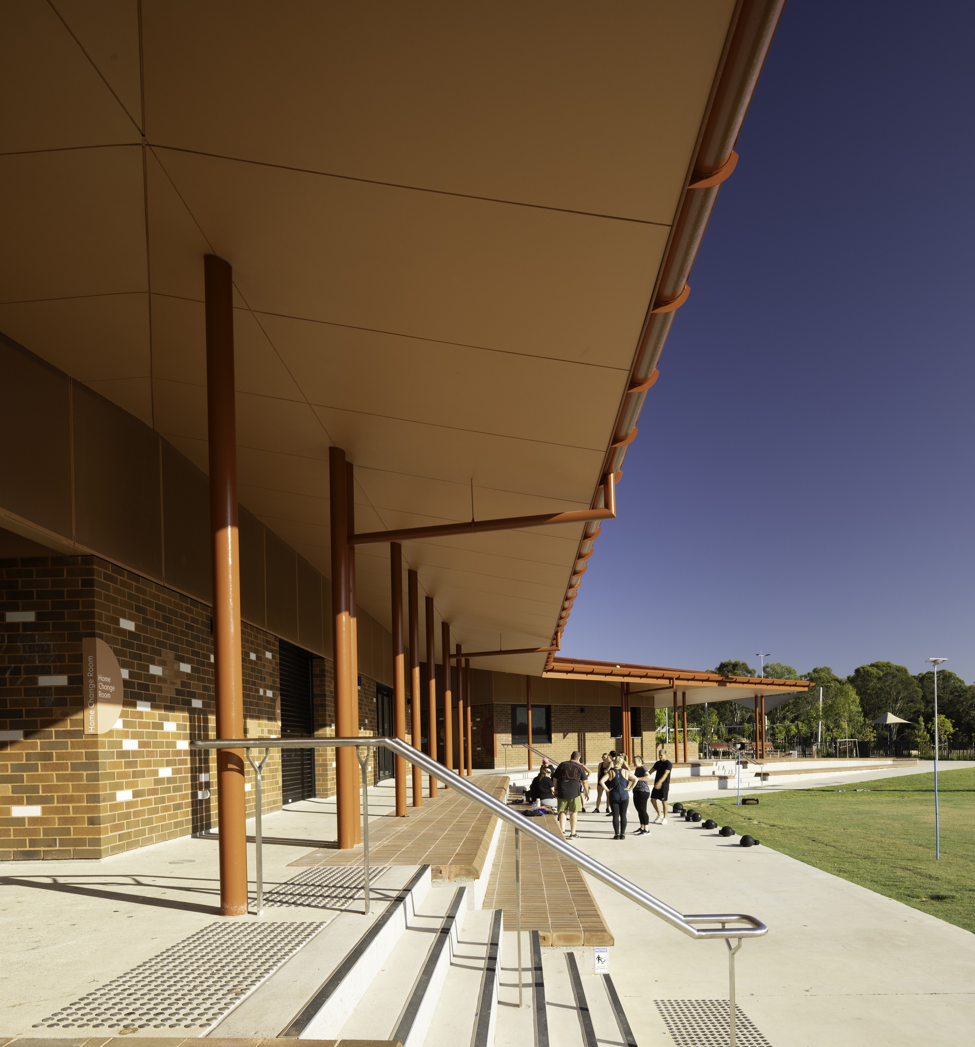 Covered walkway with steel columns and cream ceiling panels alongside variegated brick facade in shadow