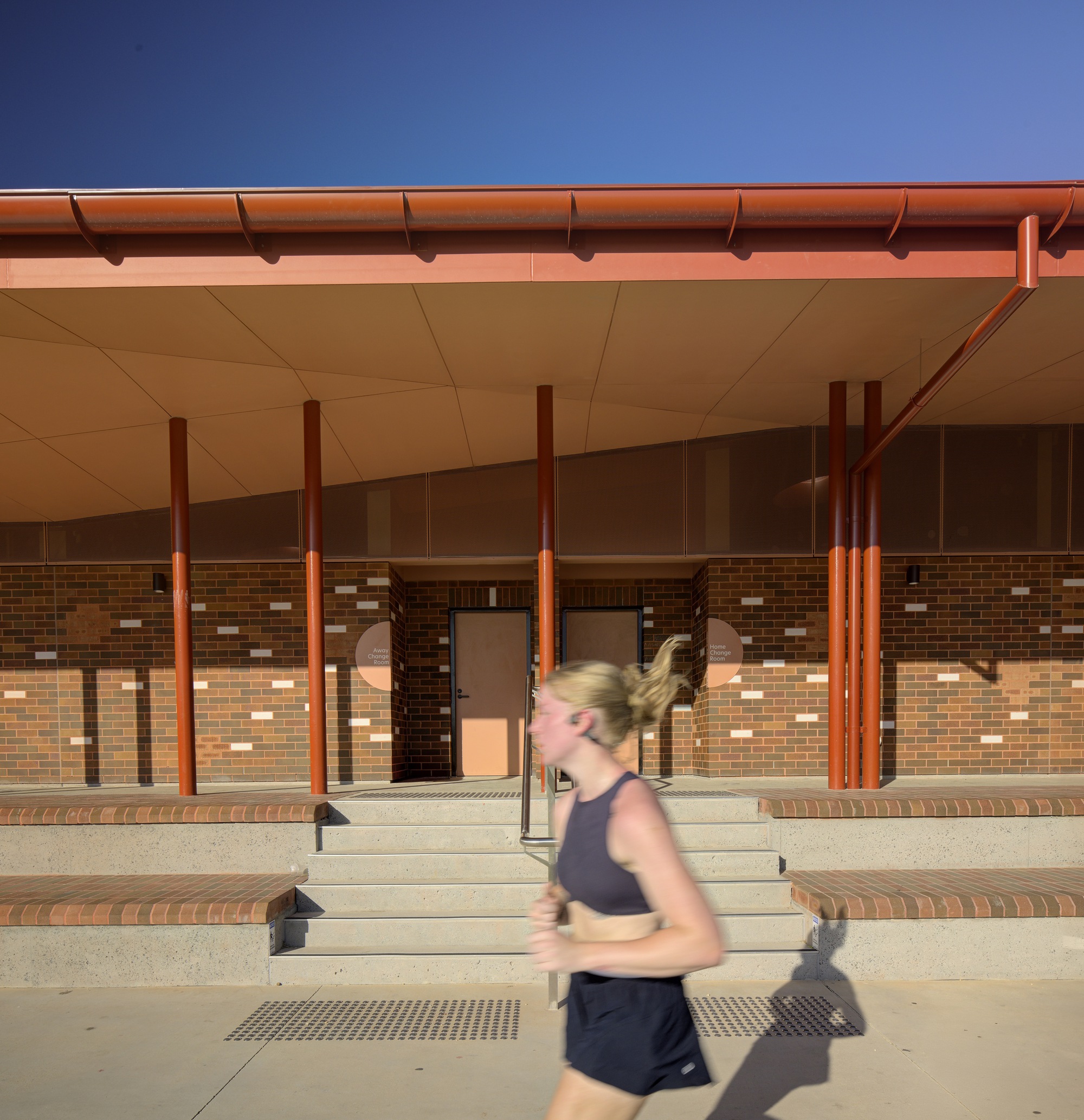 Stepped concrete entry with blurred runner passing under the red eave and gutter at dusk