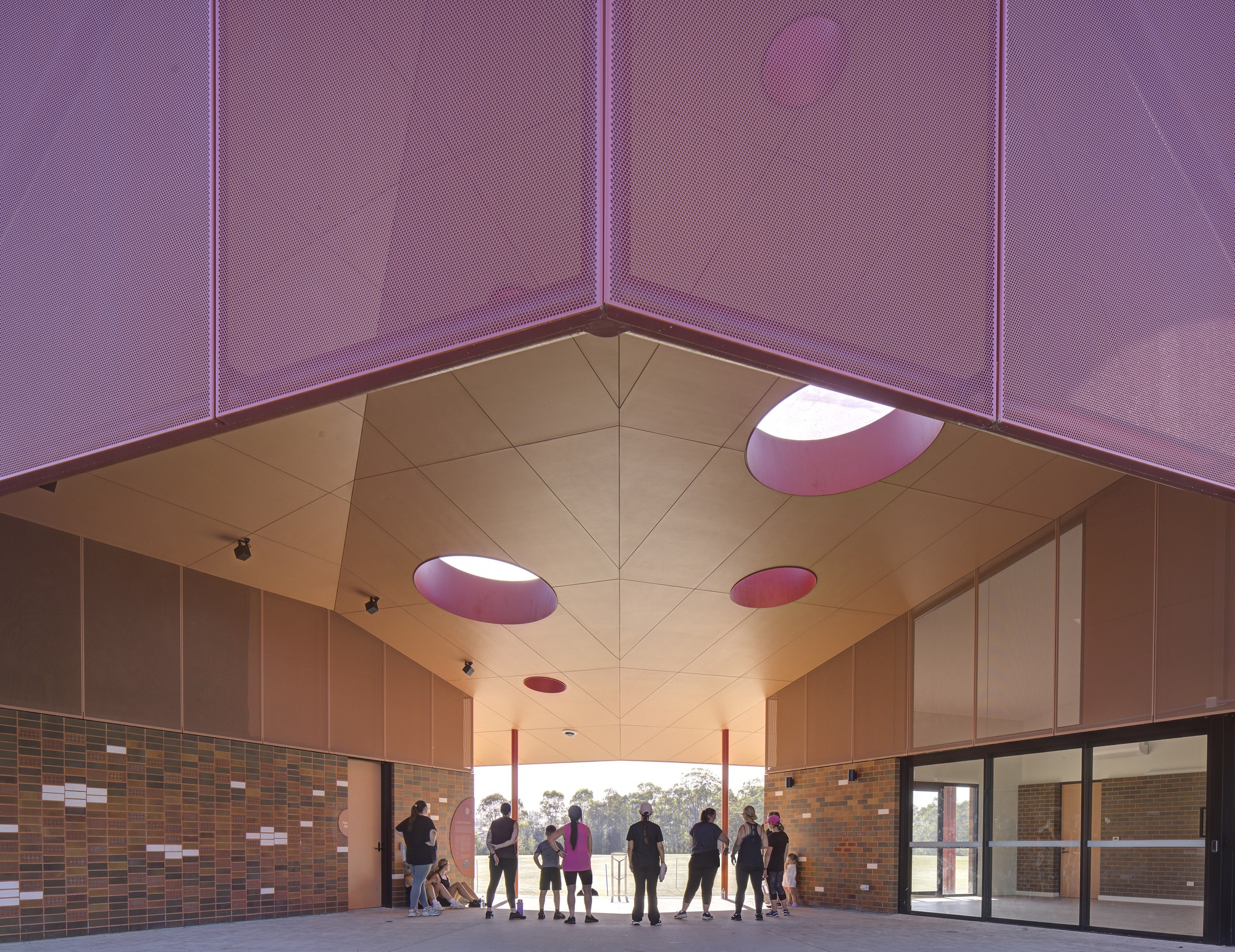 Interior gathering space with visitors silhouetted beneath vaulted ceiling with circular purple skylights