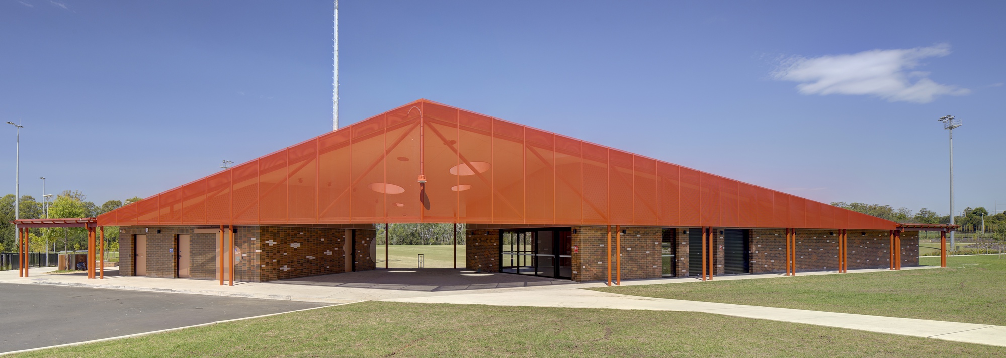 Wide low-pitched orange roof sheltering a brick colonnade under blue sky with scattered clouds