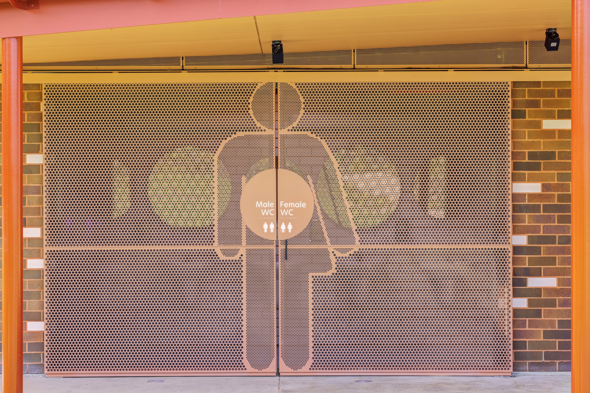 Perforated metal screen with restroom signage silhouette mounted in front of brick wall