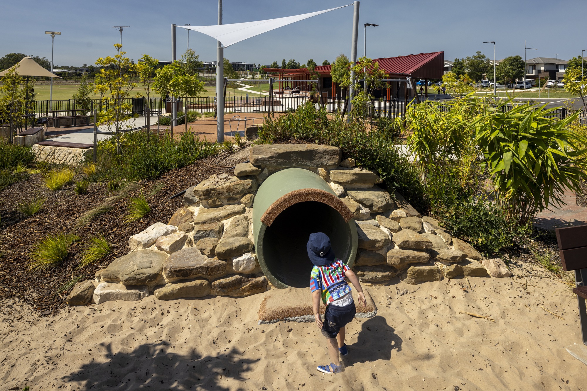 Concrete tunnel entrance surrounded by stacked sandstone boulders and native planting with a child approaching