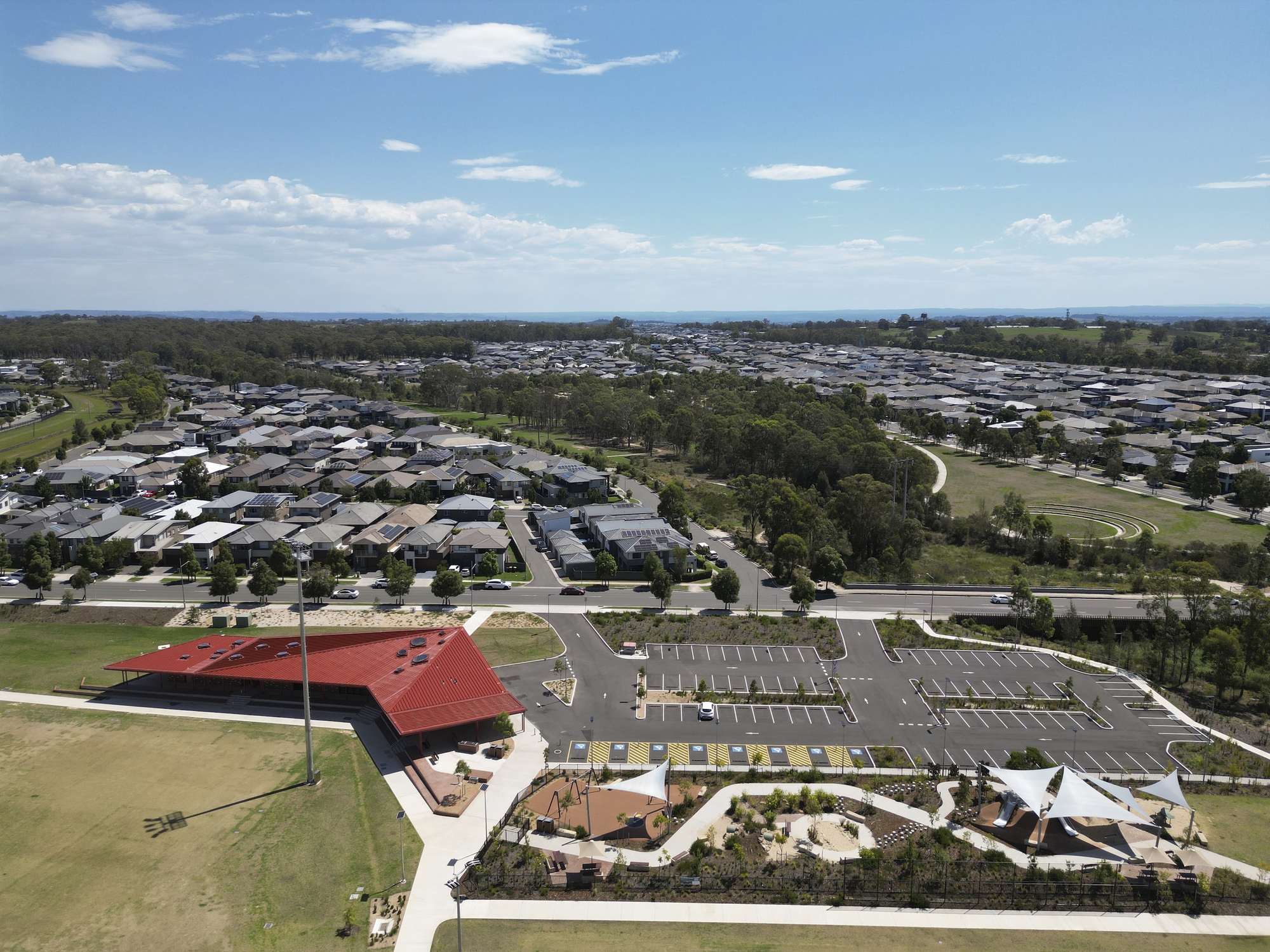 Aerial view of the red-roofed pavilion and parking area surrounded by playing fields and suburban housing