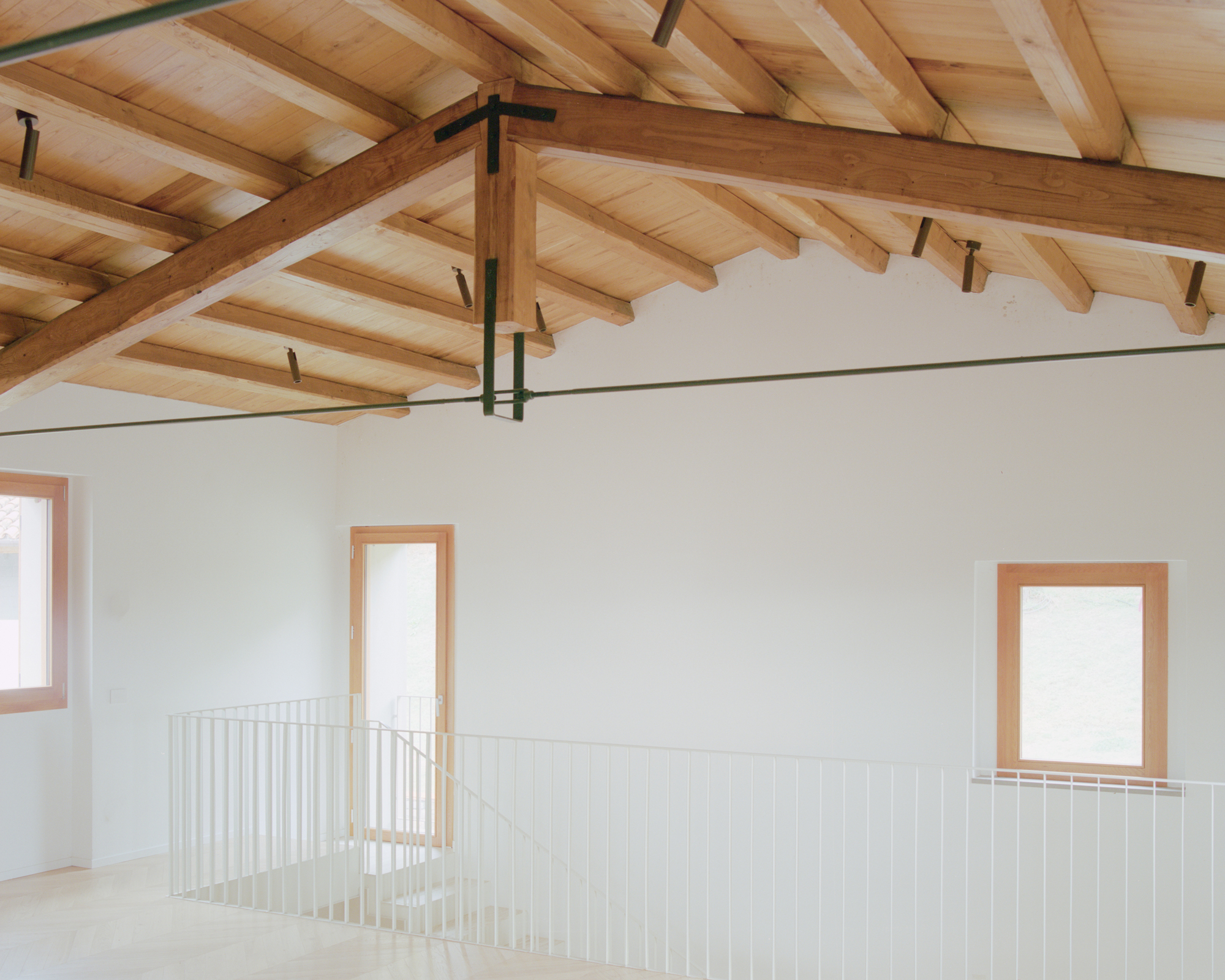 Interior view of the double-height space with exposed timber beams and white metal balustrade