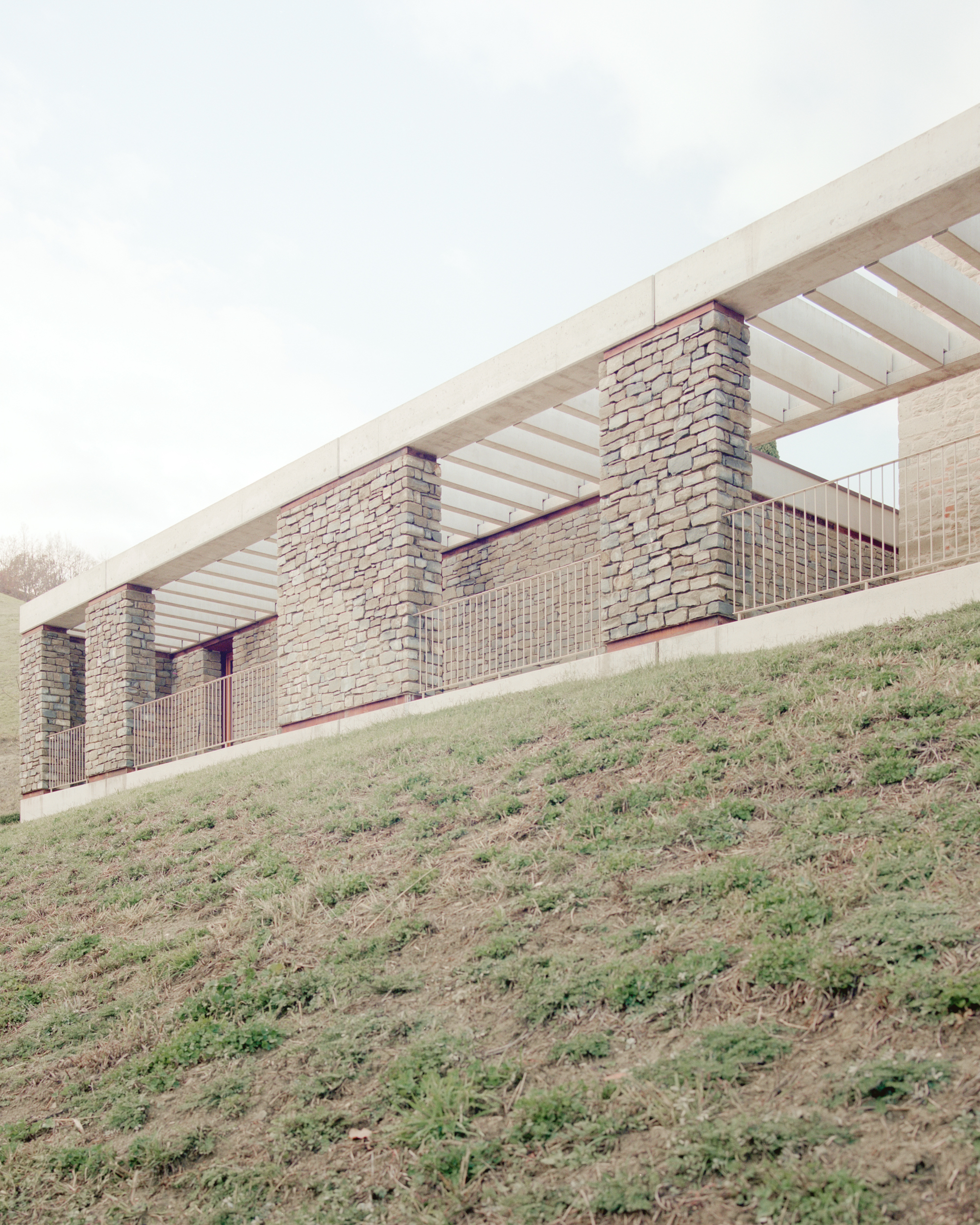 Brick facade with timber slatted roof canopy rising above a grassy hillside