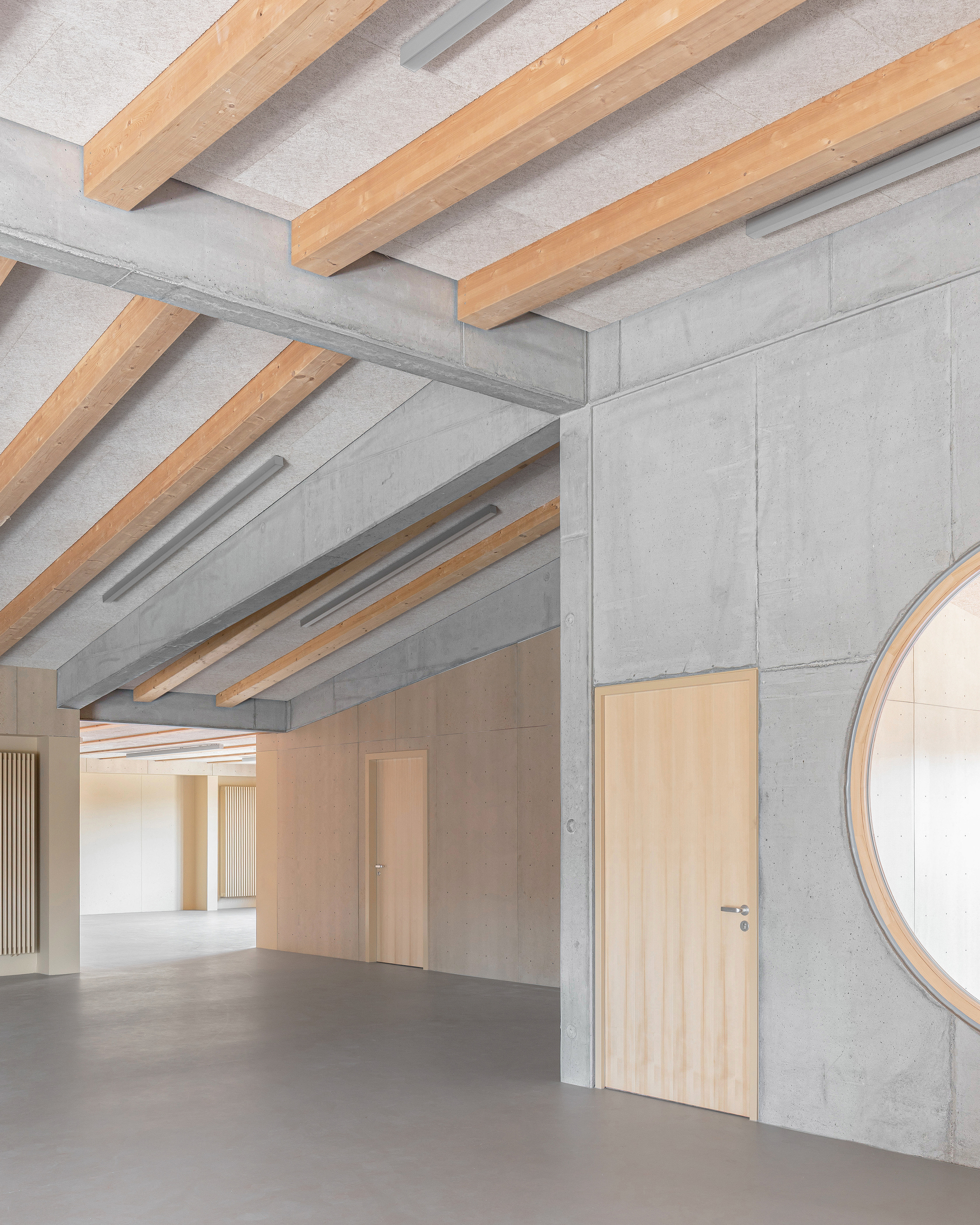 Junction of exposed timber ceiling beams meeting concrete walls with timber doors and partial circular window