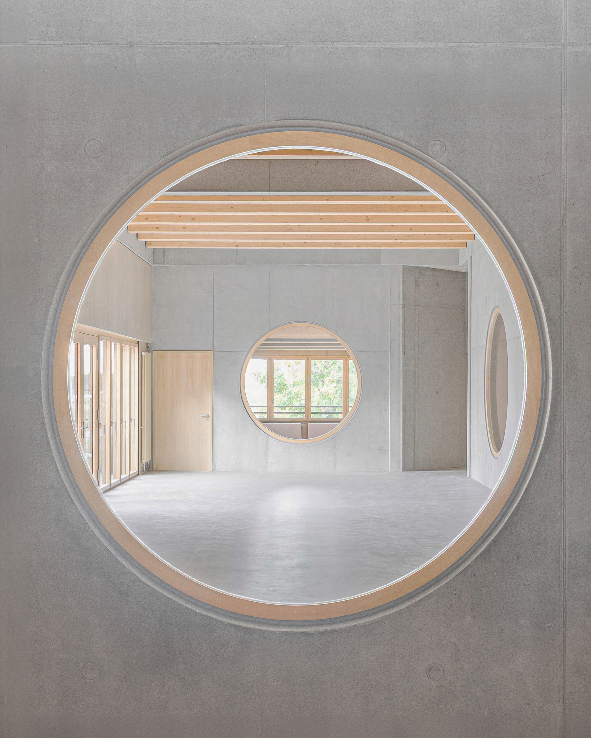 View through a circular window showing timber joists and concrete walls with nested circular openings beyond