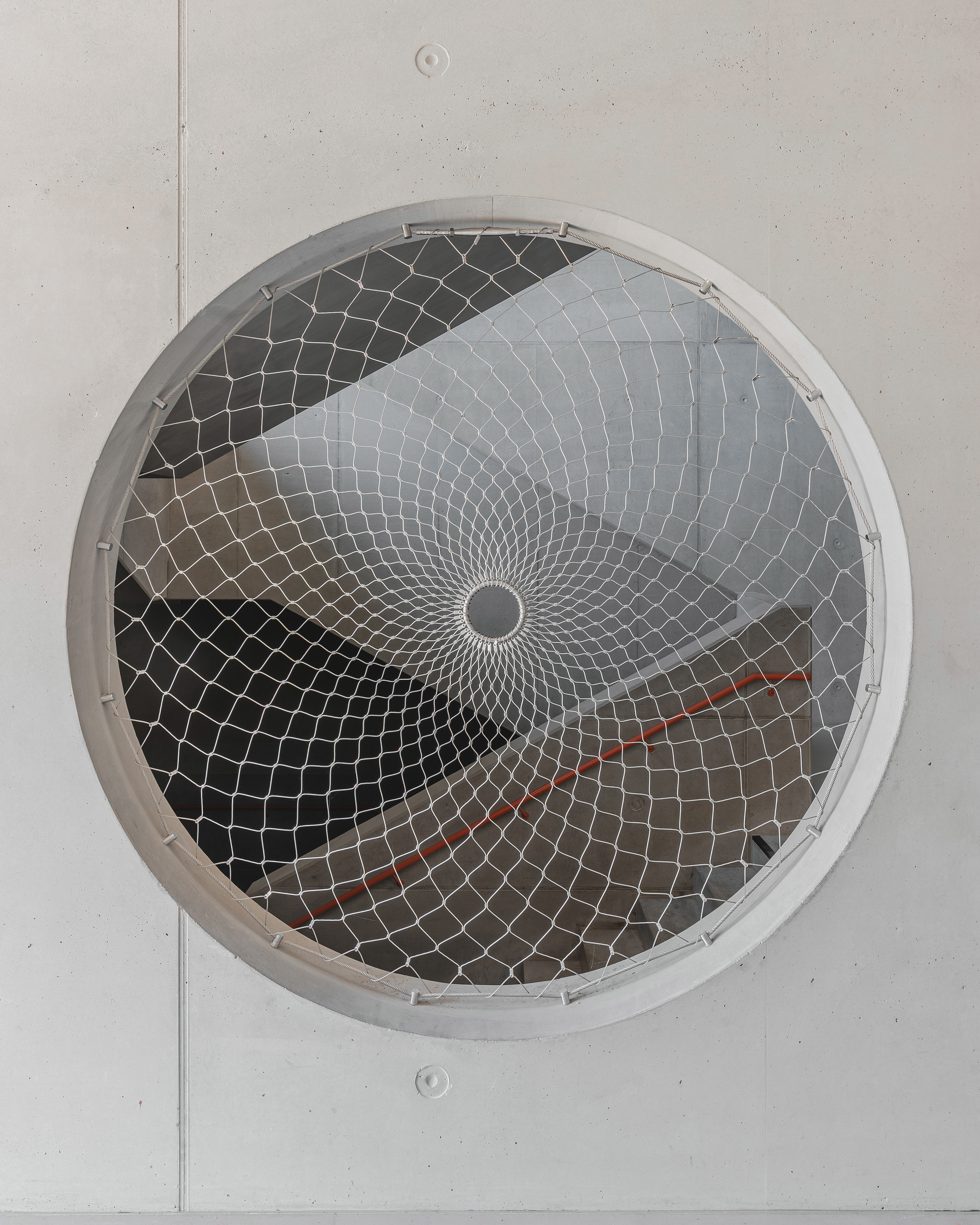 Circular ceiling vent with spiraling metal mesh guard in a light grey panel