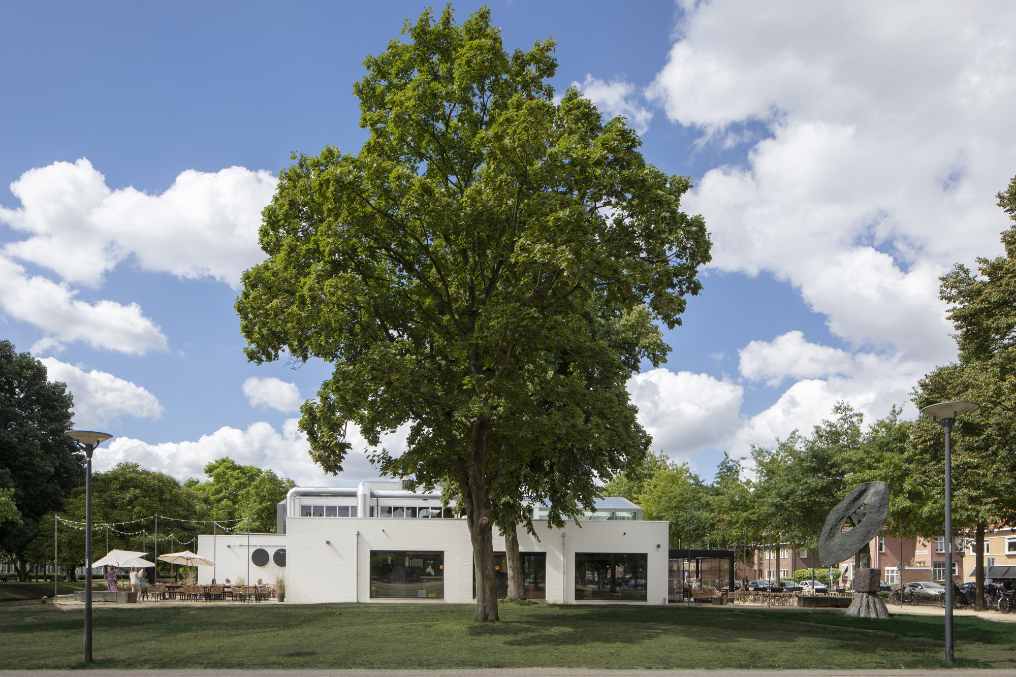 White pavilion with porthole windows and clerestory glazing set in a lawn beneath a mature oak tree