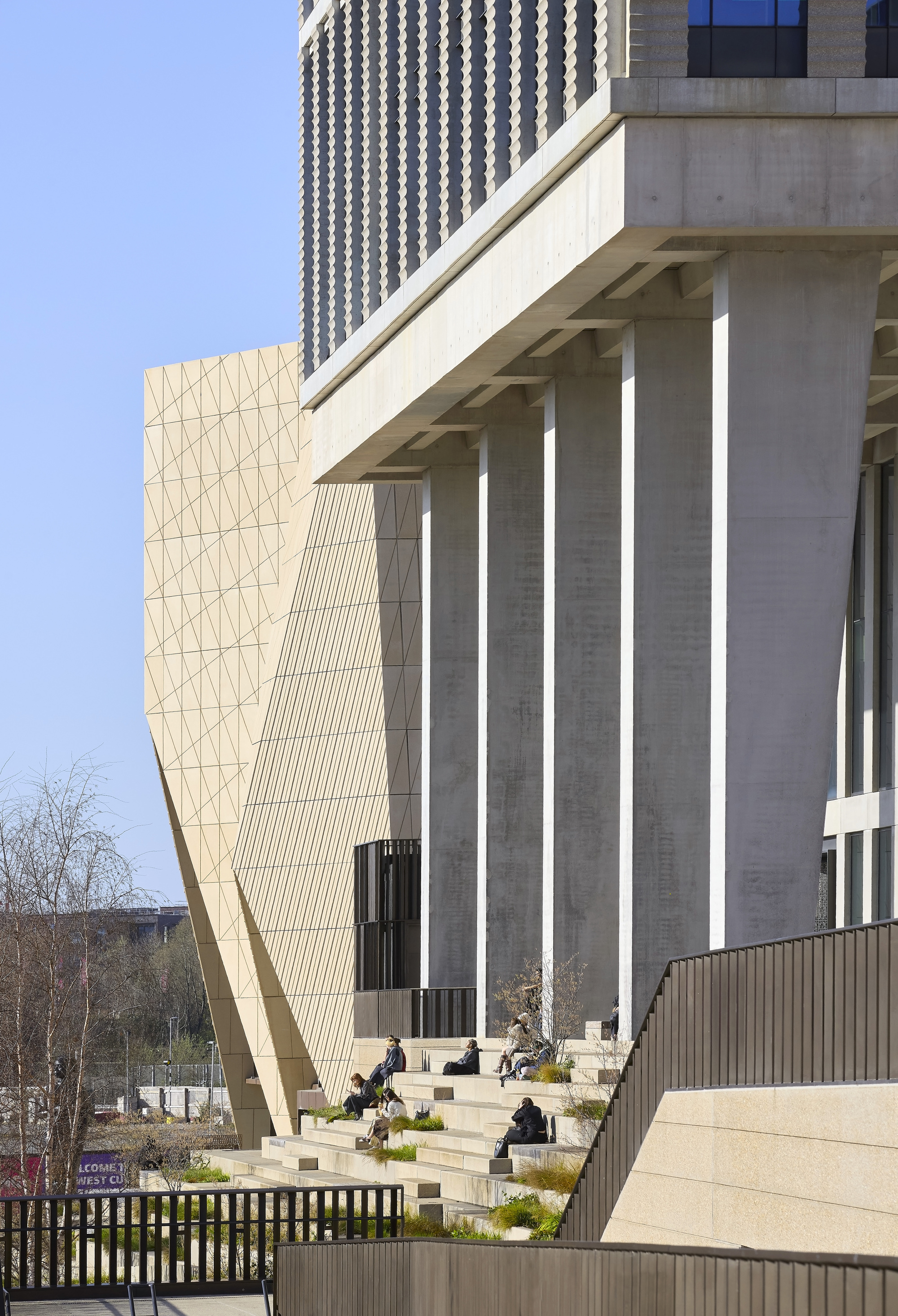 Concrete colonnade at ground level with visitors seated on planted terraces beside the sculptural facade