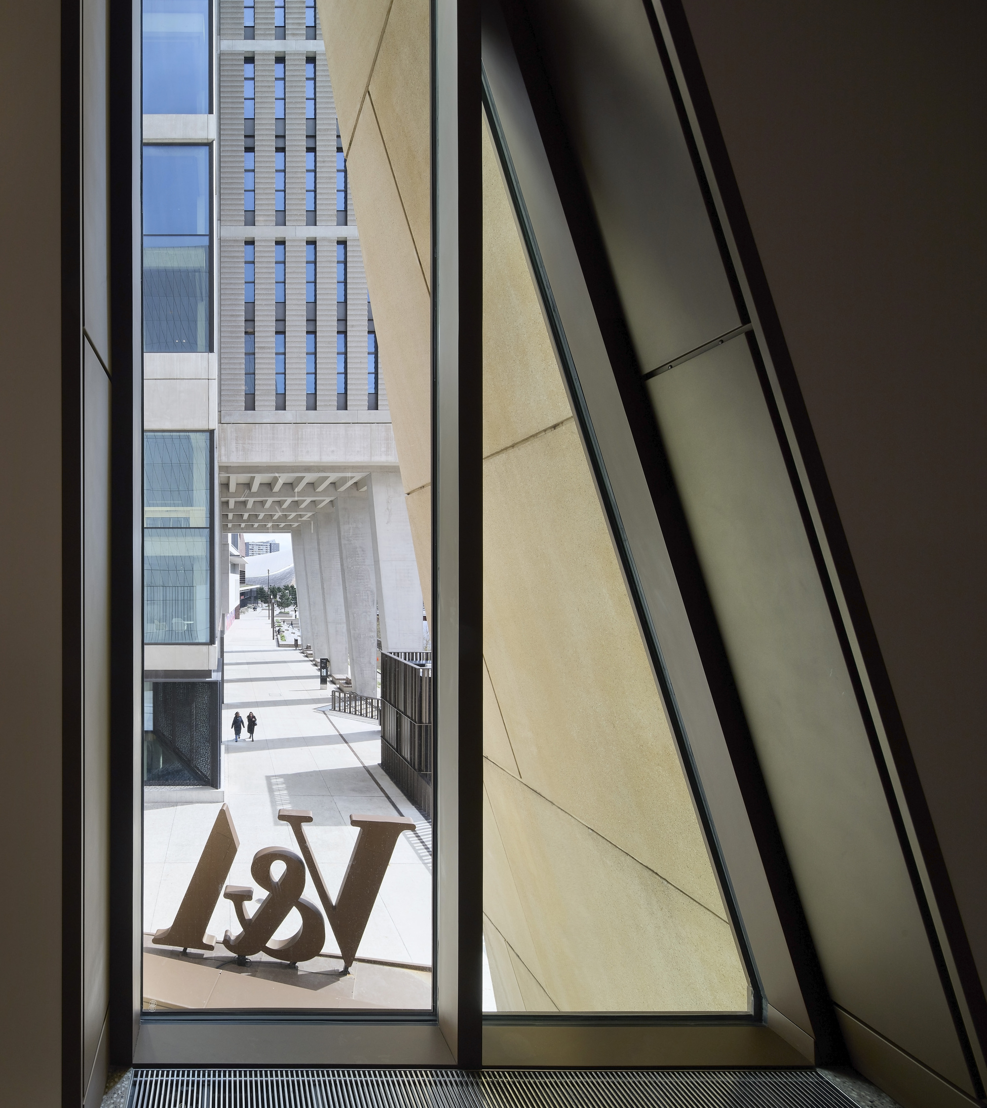 Angled window framing a view of the courtyard with chequered tower facade and pedestrians in bright daylight
