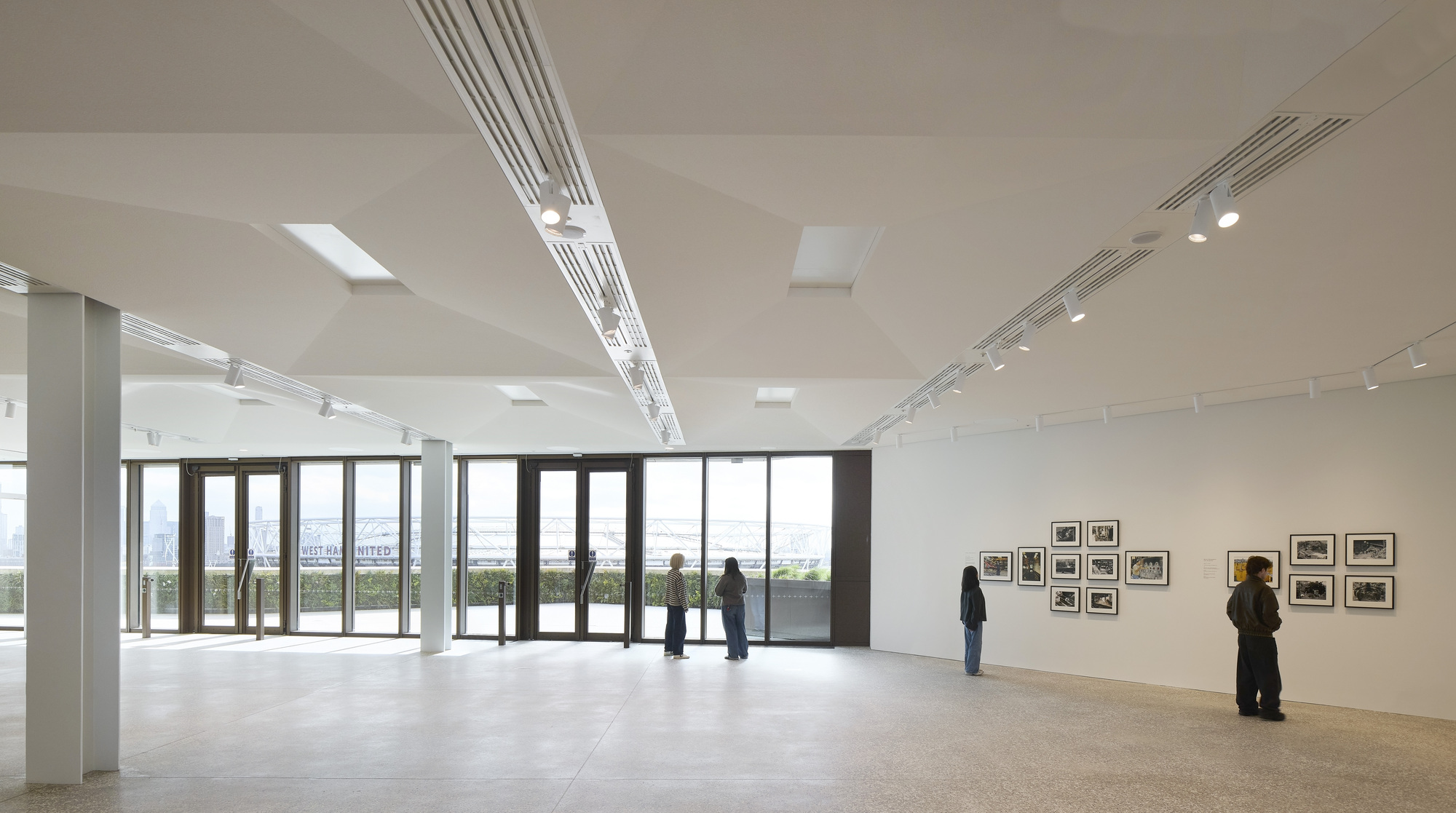Gallery space with polished concrete floor and visitors viewing framed photographs along white walls