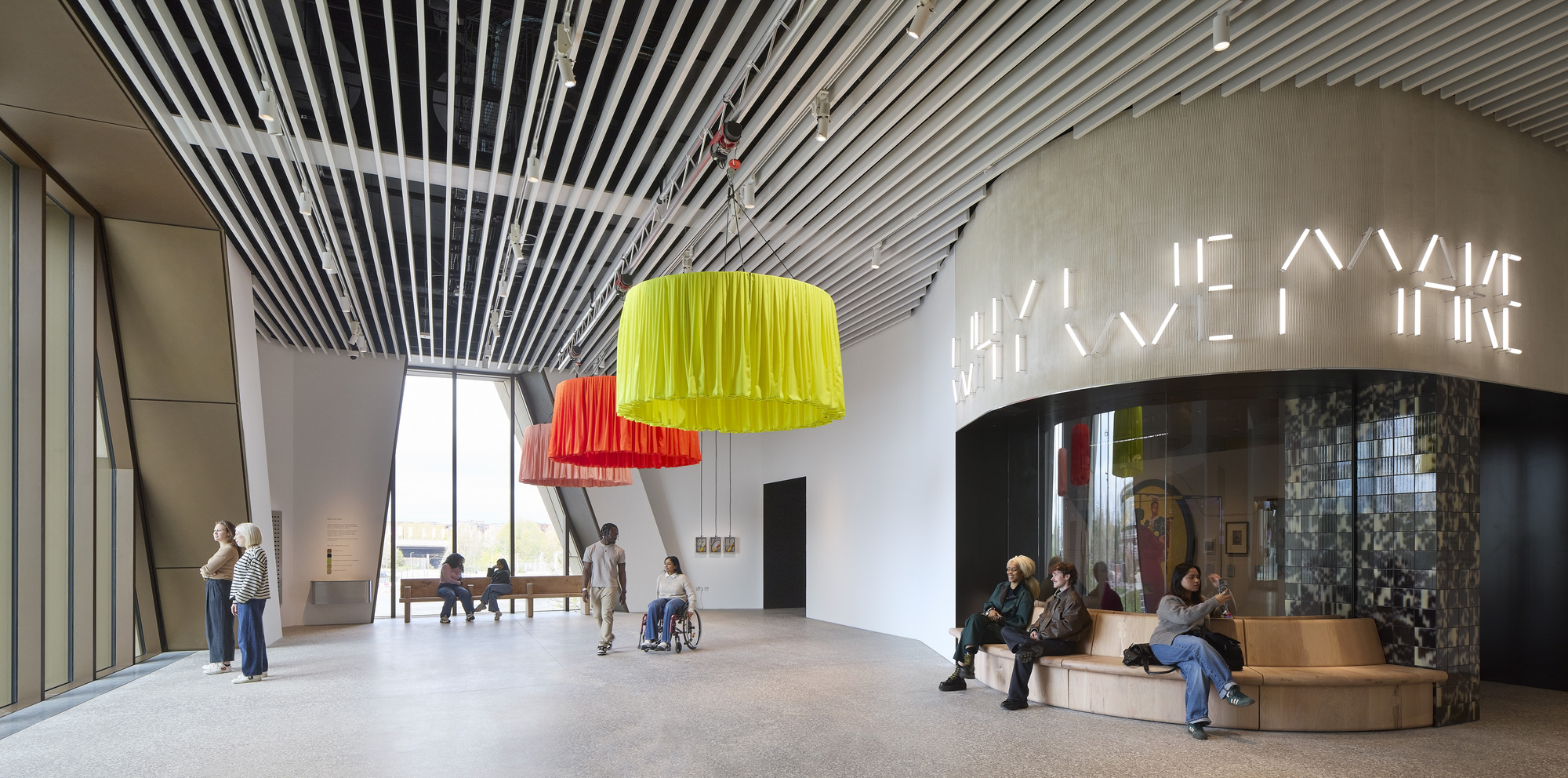 Double-height foyer with yellow and orange pendant lights and visitors beneath curved slatted ceiling