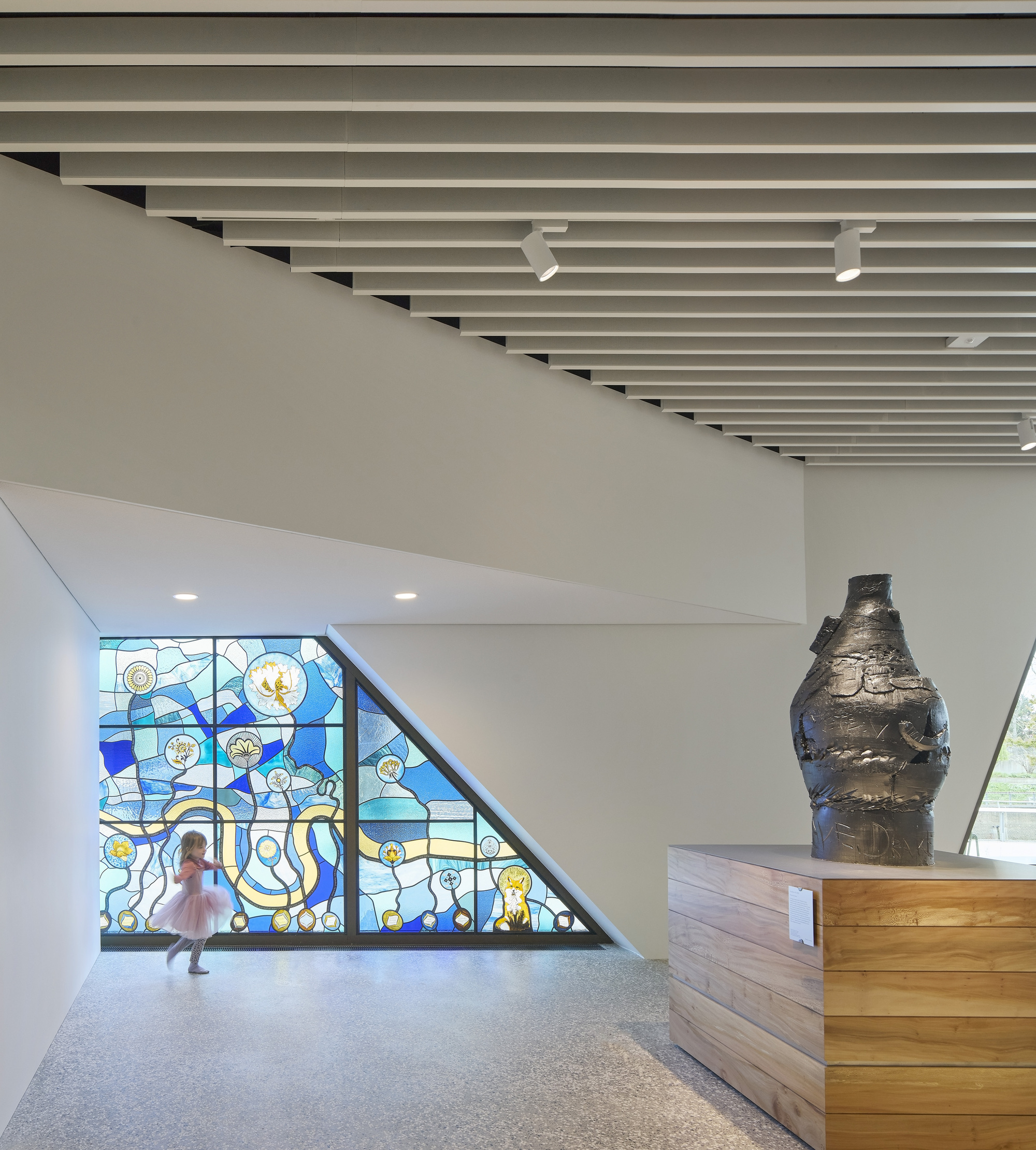 Stained glass window fills triangular wall beside timber reception desk and terrazzo floor