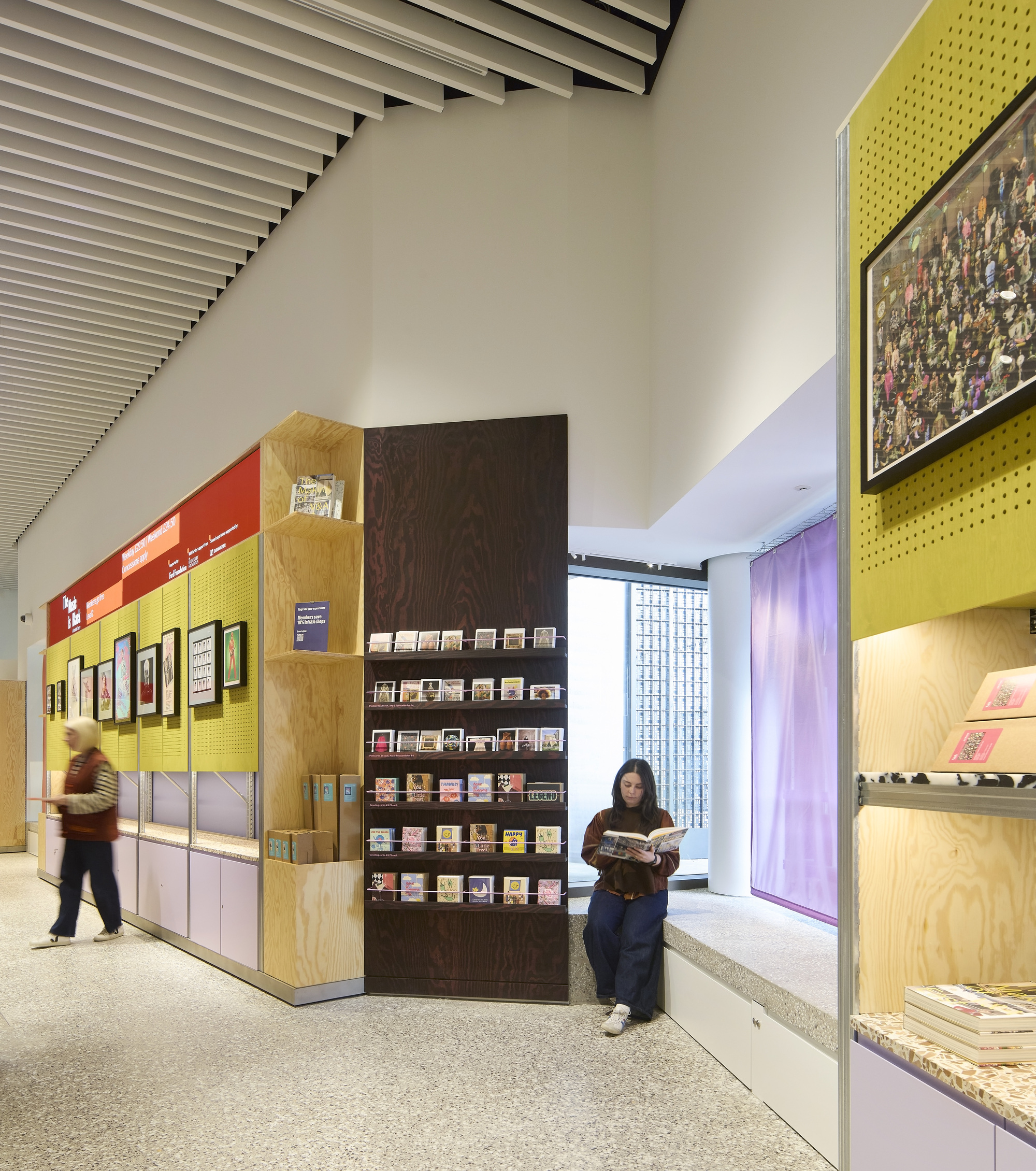 Visitor reading beside freestanding display wall with yellow pegboard and plywood shelving