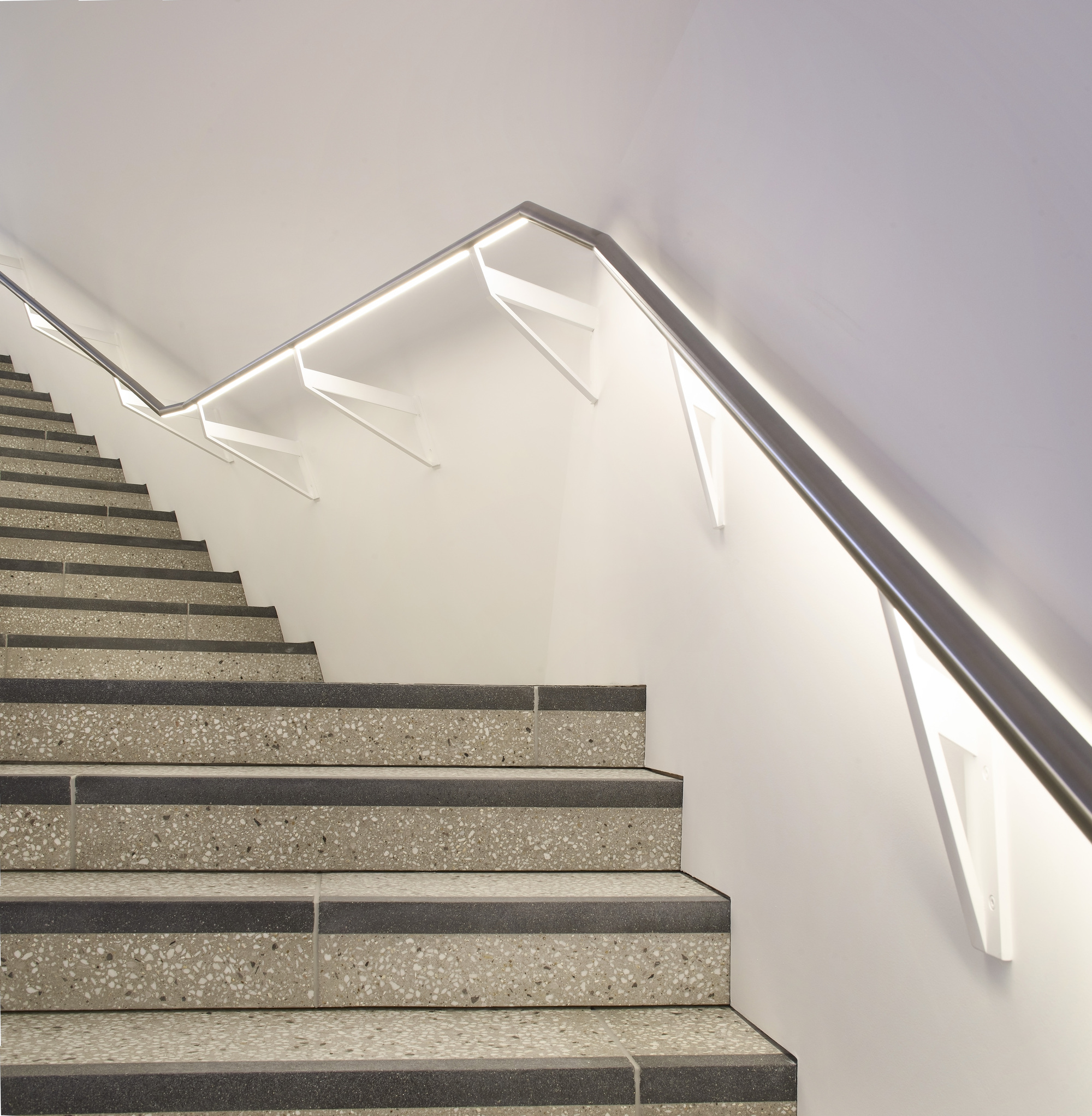 Close-up of the folded metal handrail with integrated LED strip along the terrazzo stair flights