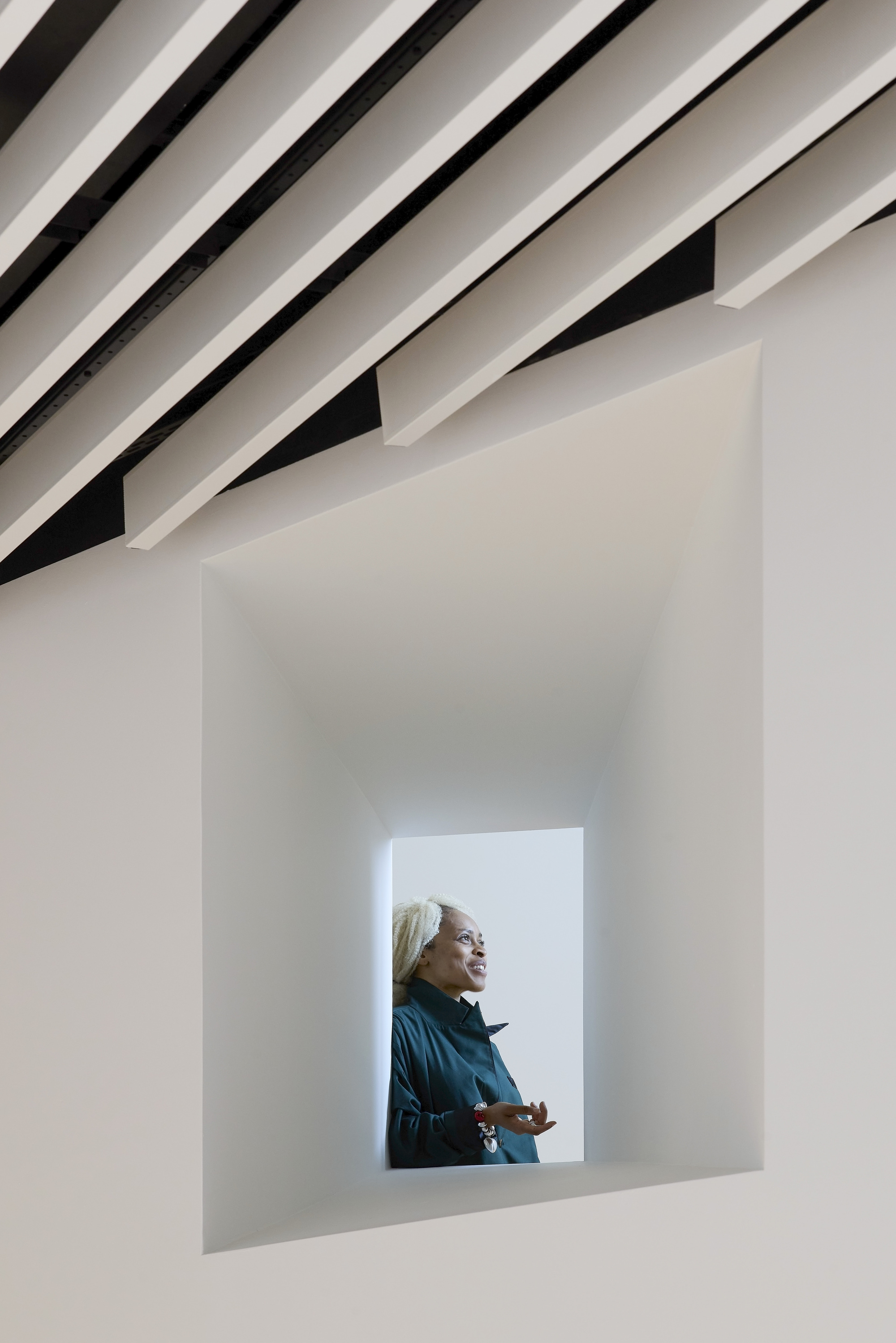 Deep framed window opening with a visitor looking outward beneath angled ceiling louvers