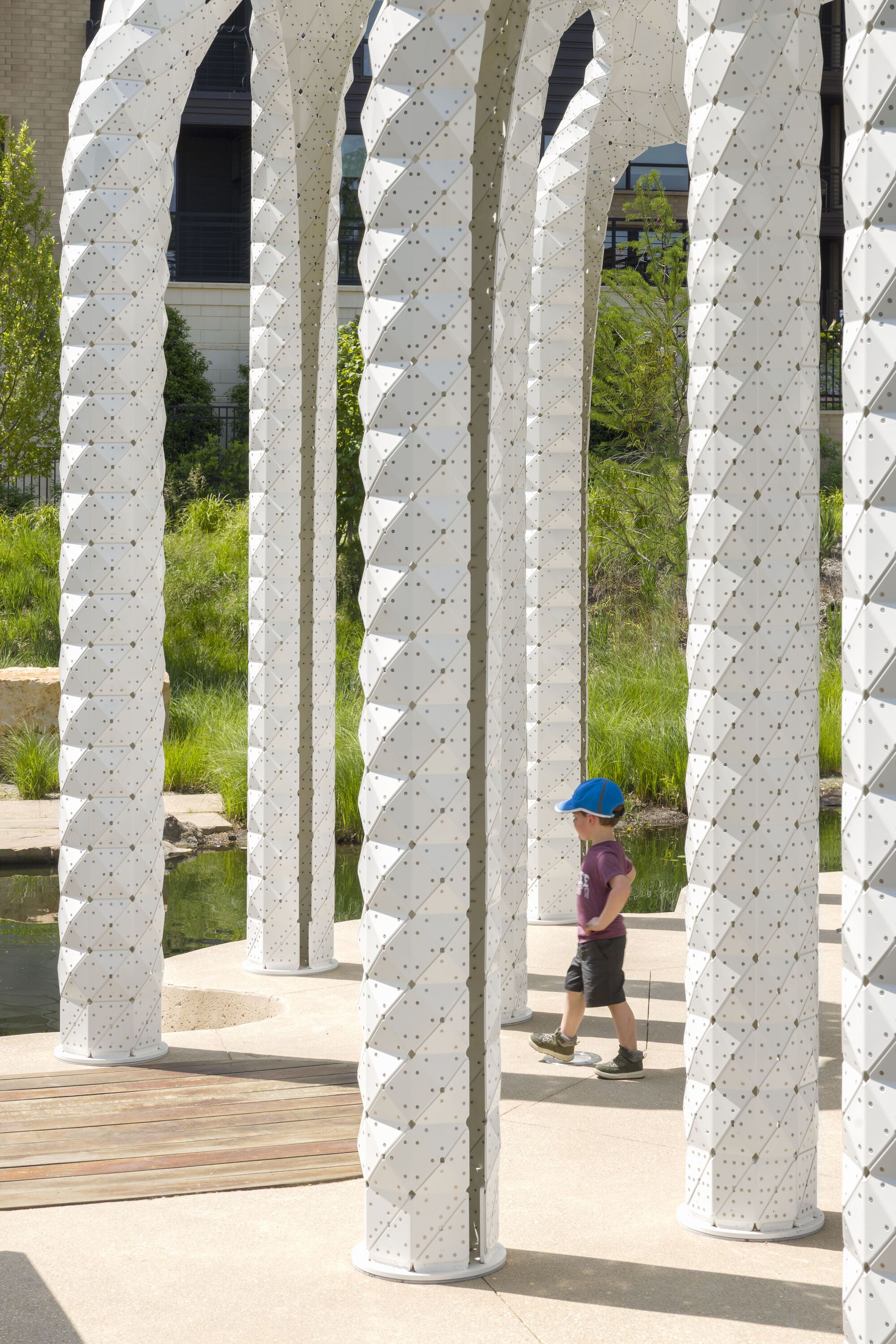 Close view through textured white columns with child in blue cap walking on timber decking