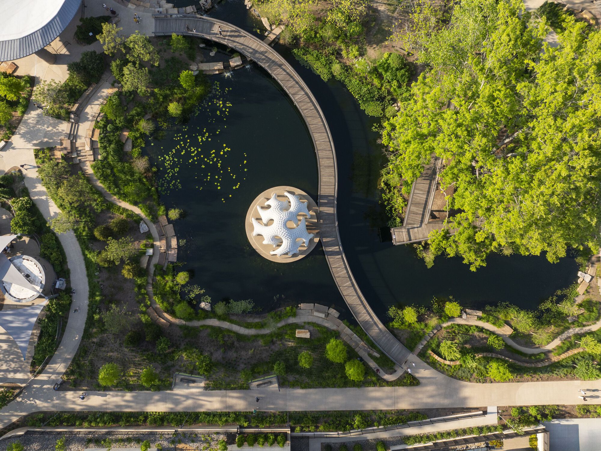 Drone view of circular pavilion in pond surrounded by curving boardwalks and landscape planting
