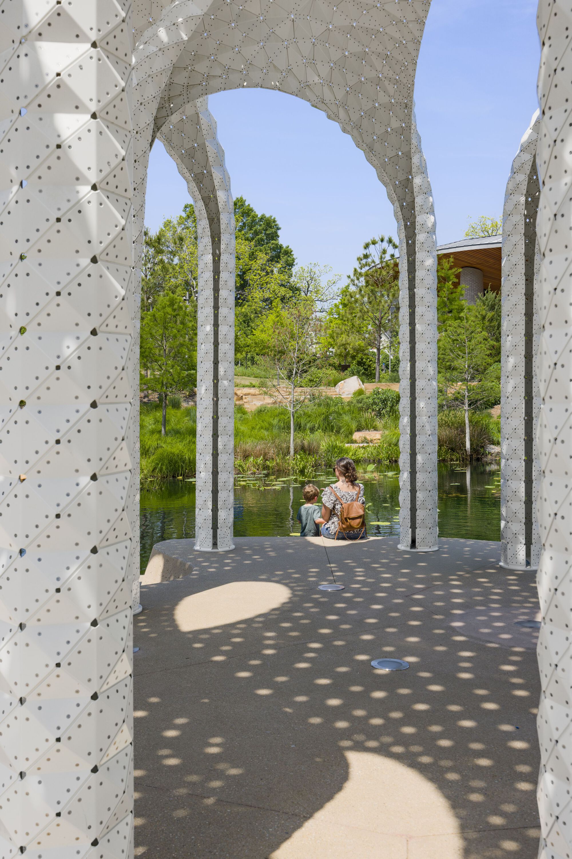 View through arched openings with visitors seated on the pavilion floor overlooking the pond