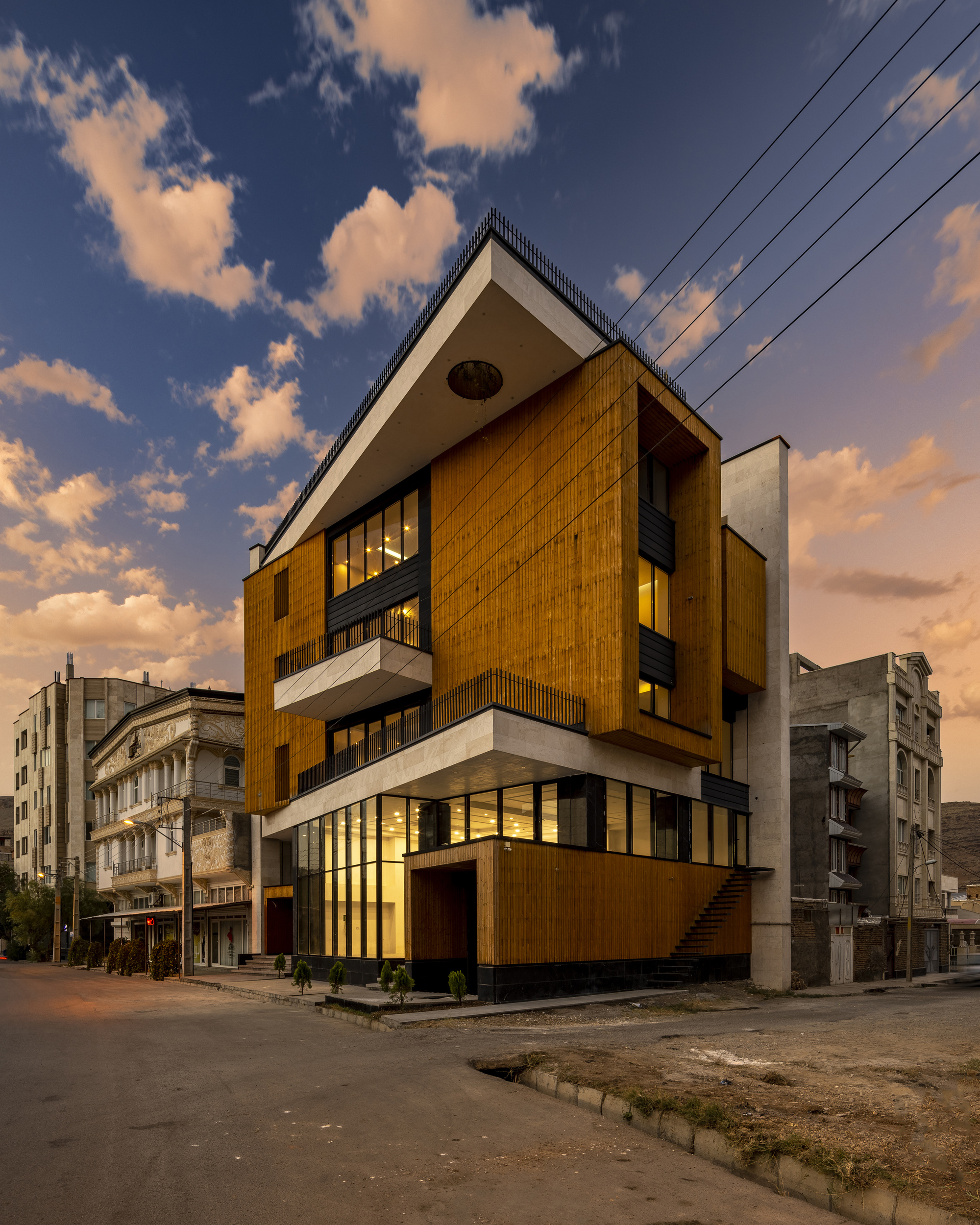 Corner view at sunset showing the angled timber-clad facade and projecting white balconies