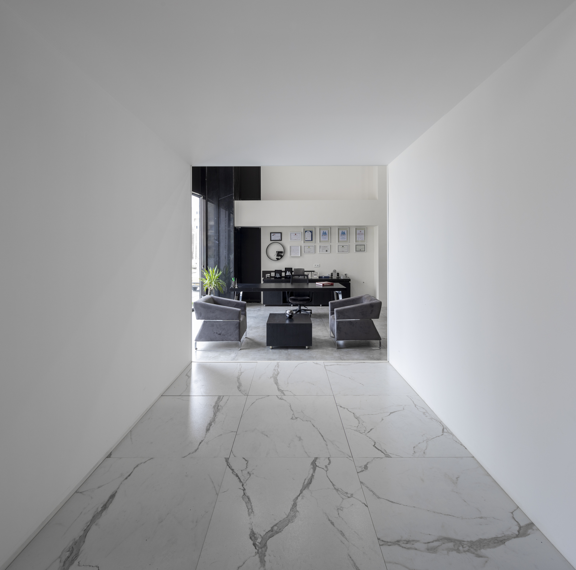 White corridor with veined marble tile floor leading to a seating area with framed artworks