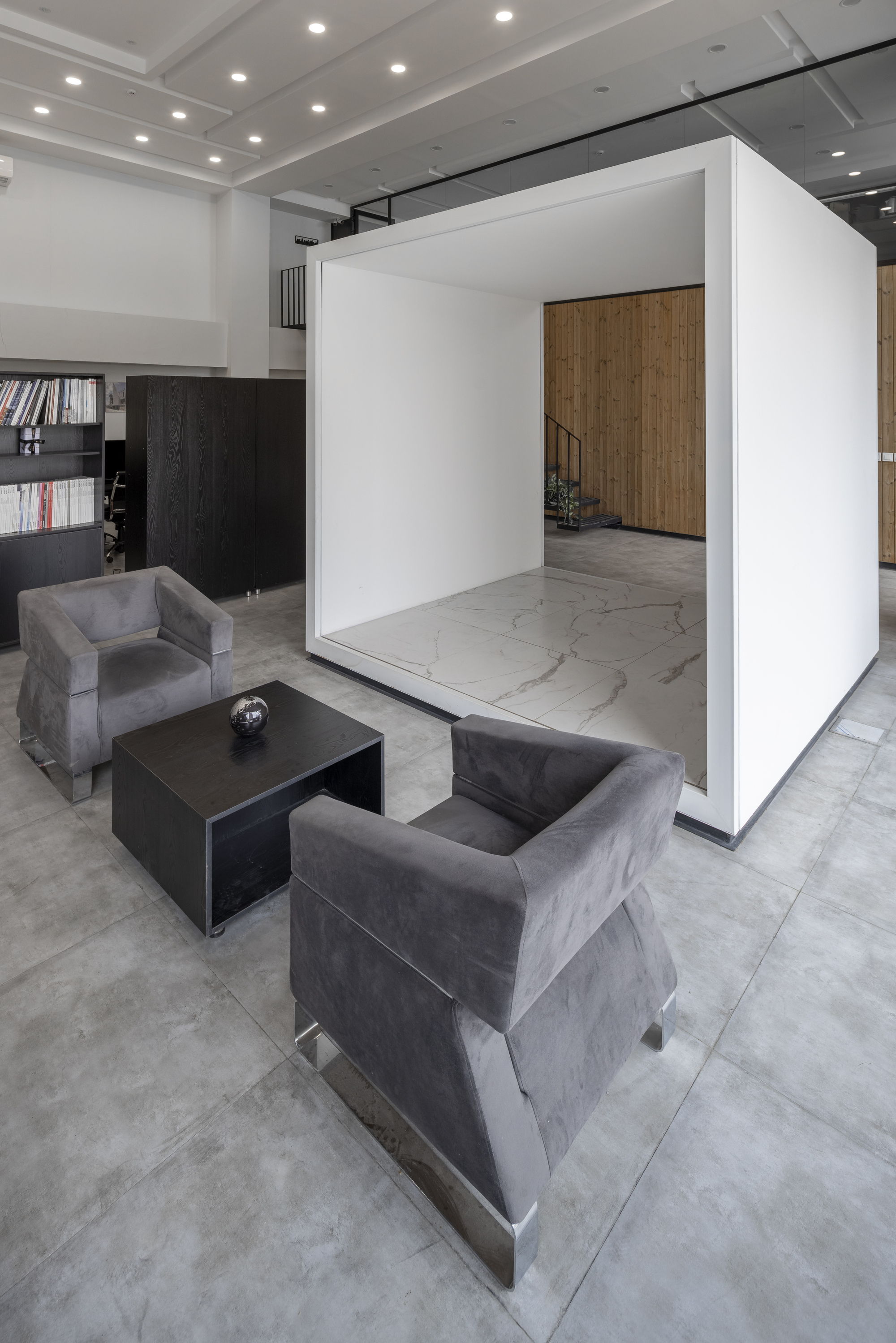 Freestanding white box volume with marble floor framing a view to timber-clad staircase beyond