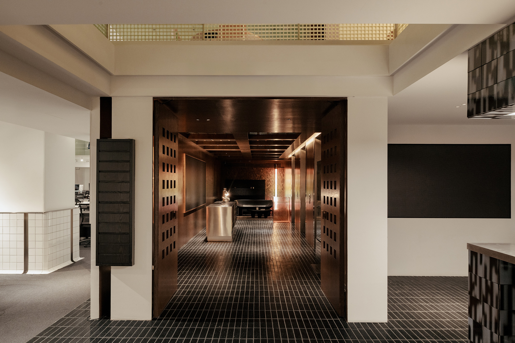 View through double doors into a timber-lined corridor from a white reception area with gridded skylights