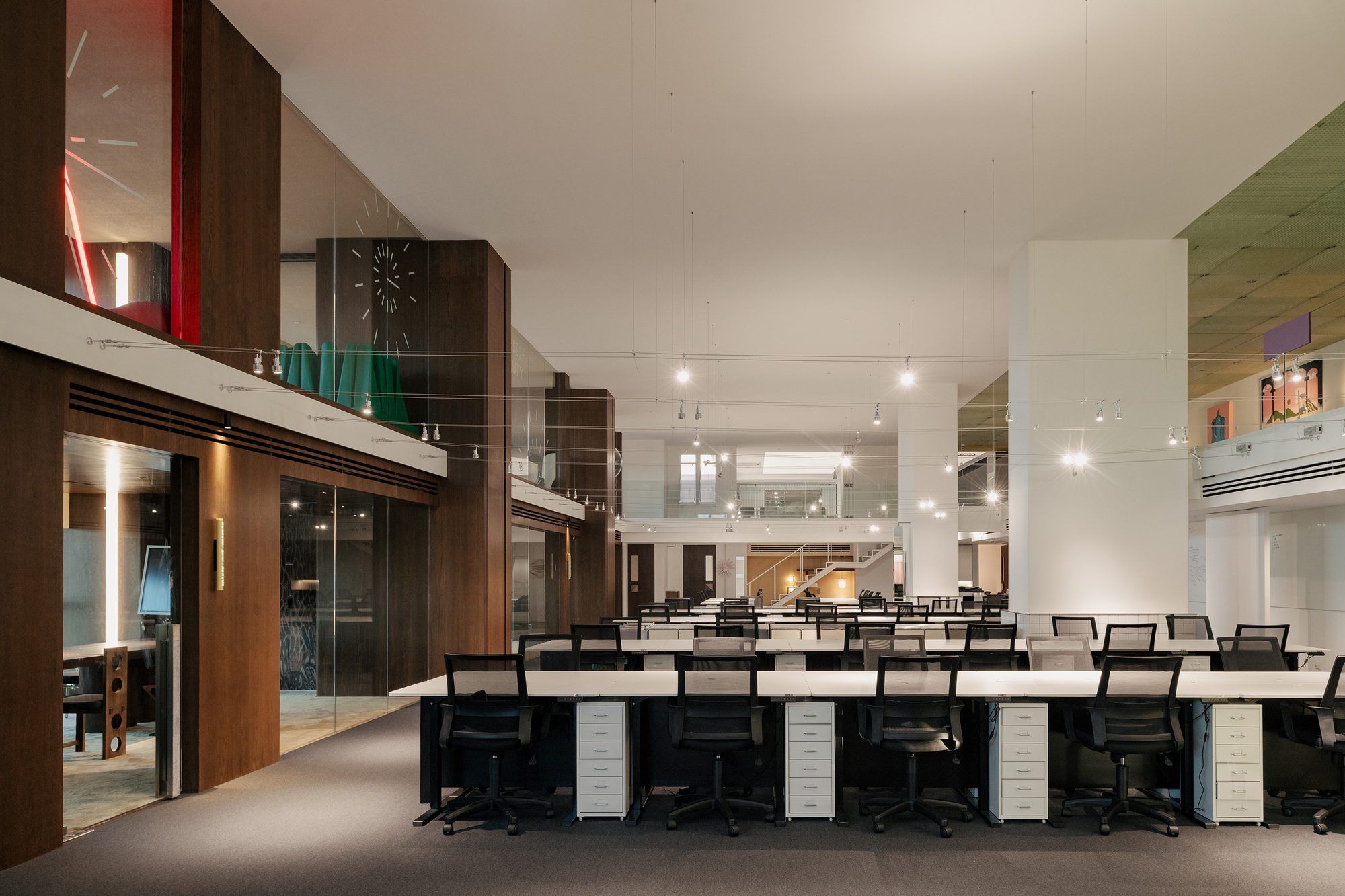 Open-plan office area with rows of workstations beneath a mezzanine and track lighting overhead