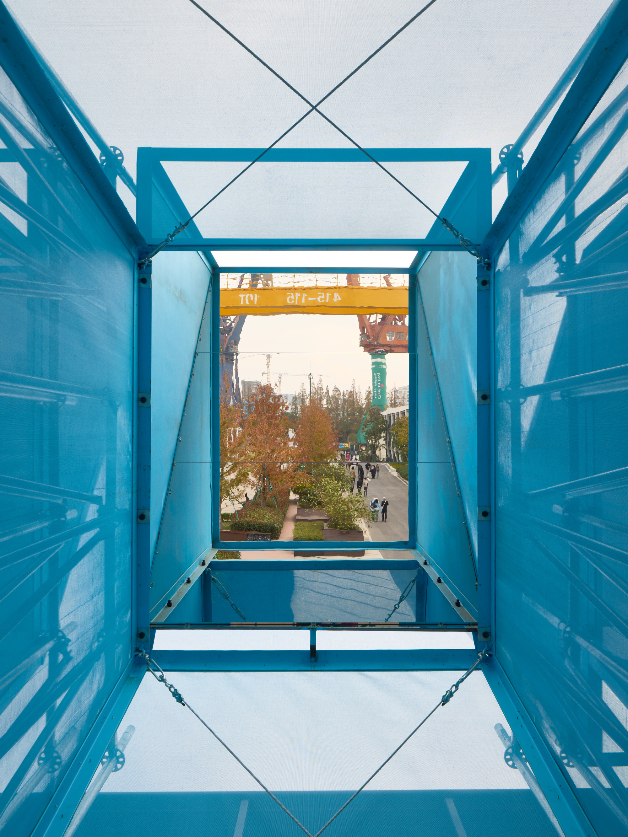View through blue shipping container structure showing metal framing and distant construction cranes