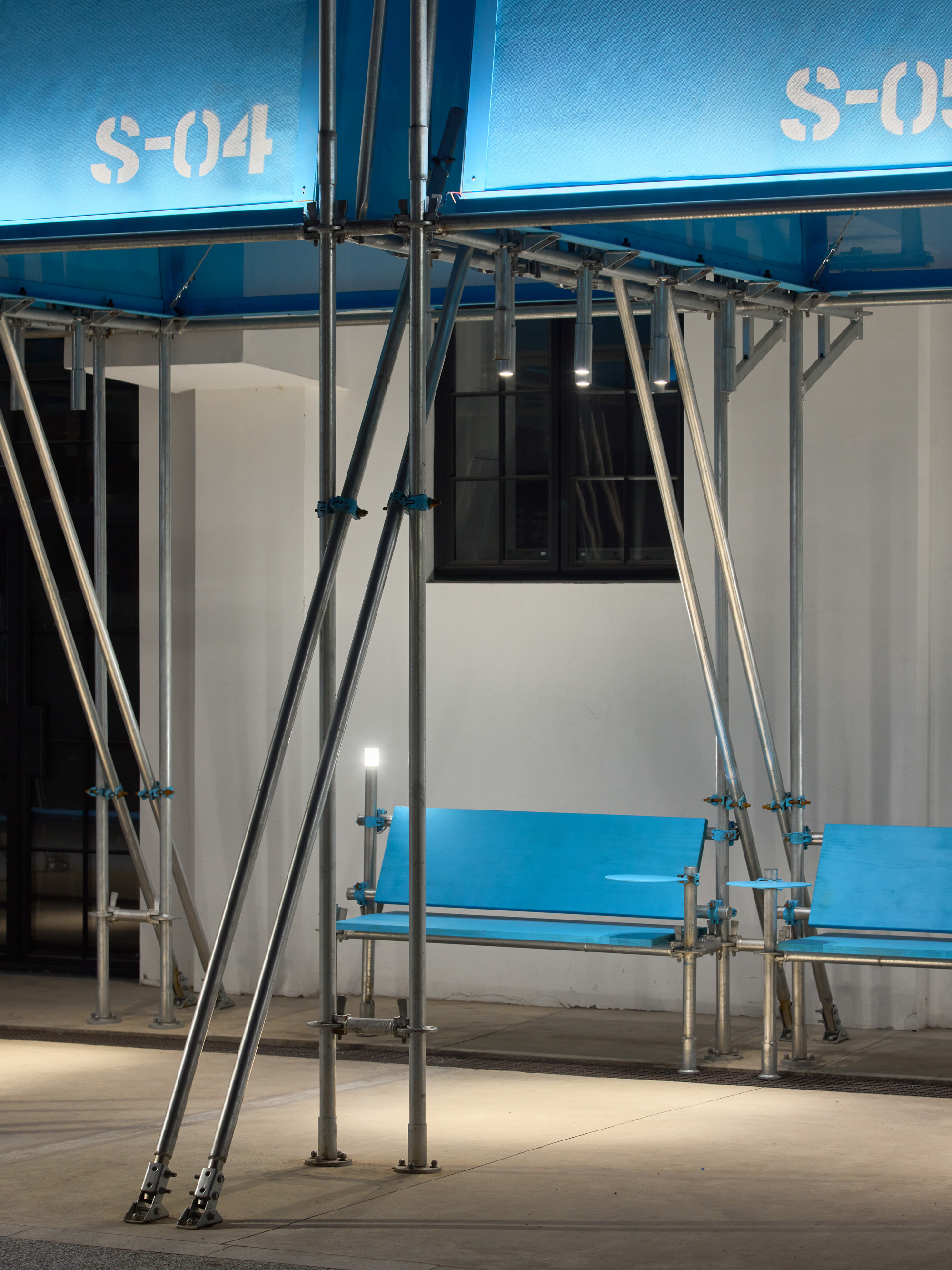 Steel scaffolding swing structure in front of blue and white modular units at dusk