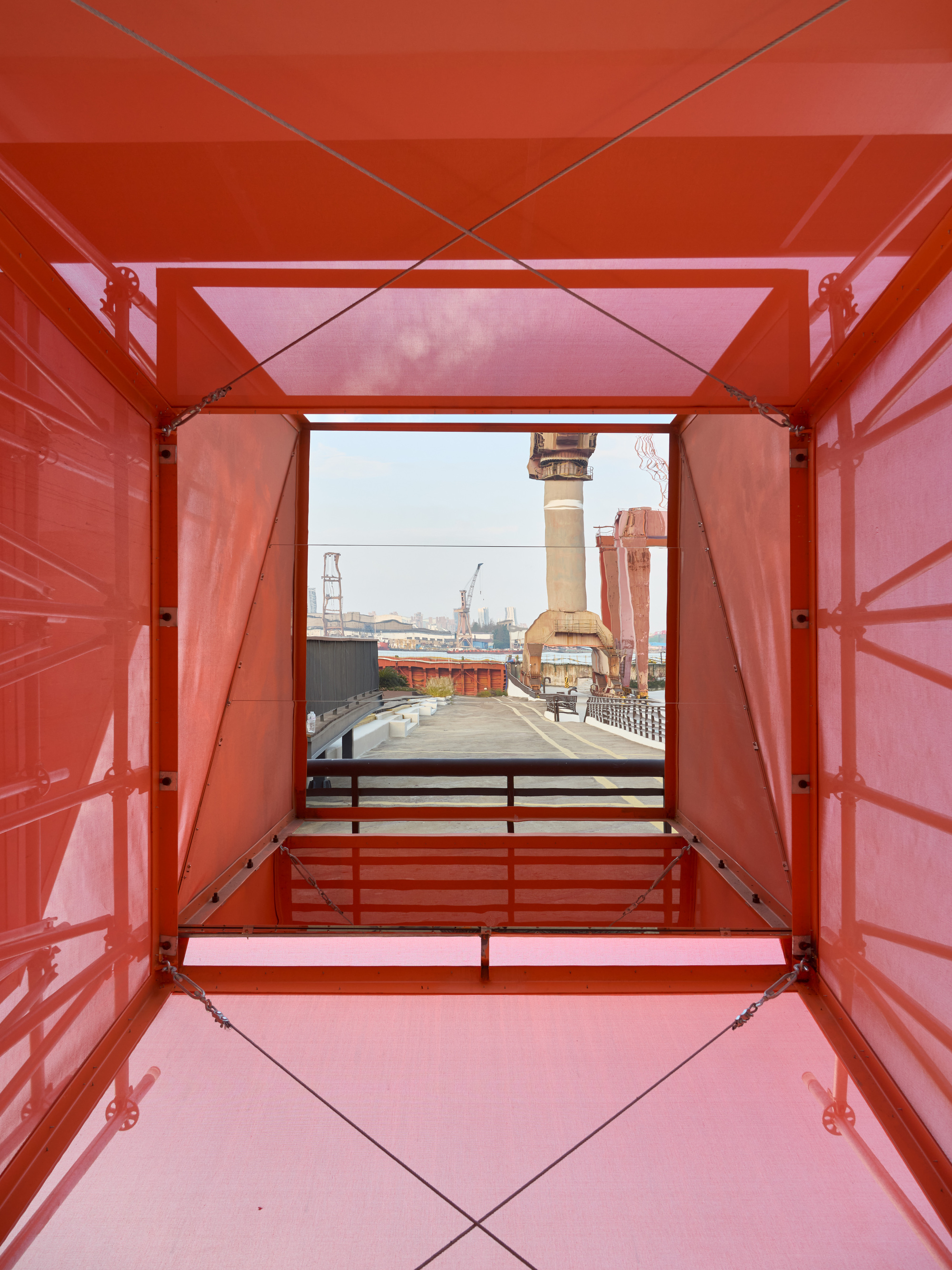 View through orange metal container frame toward shipyard crane and industrial waterfront