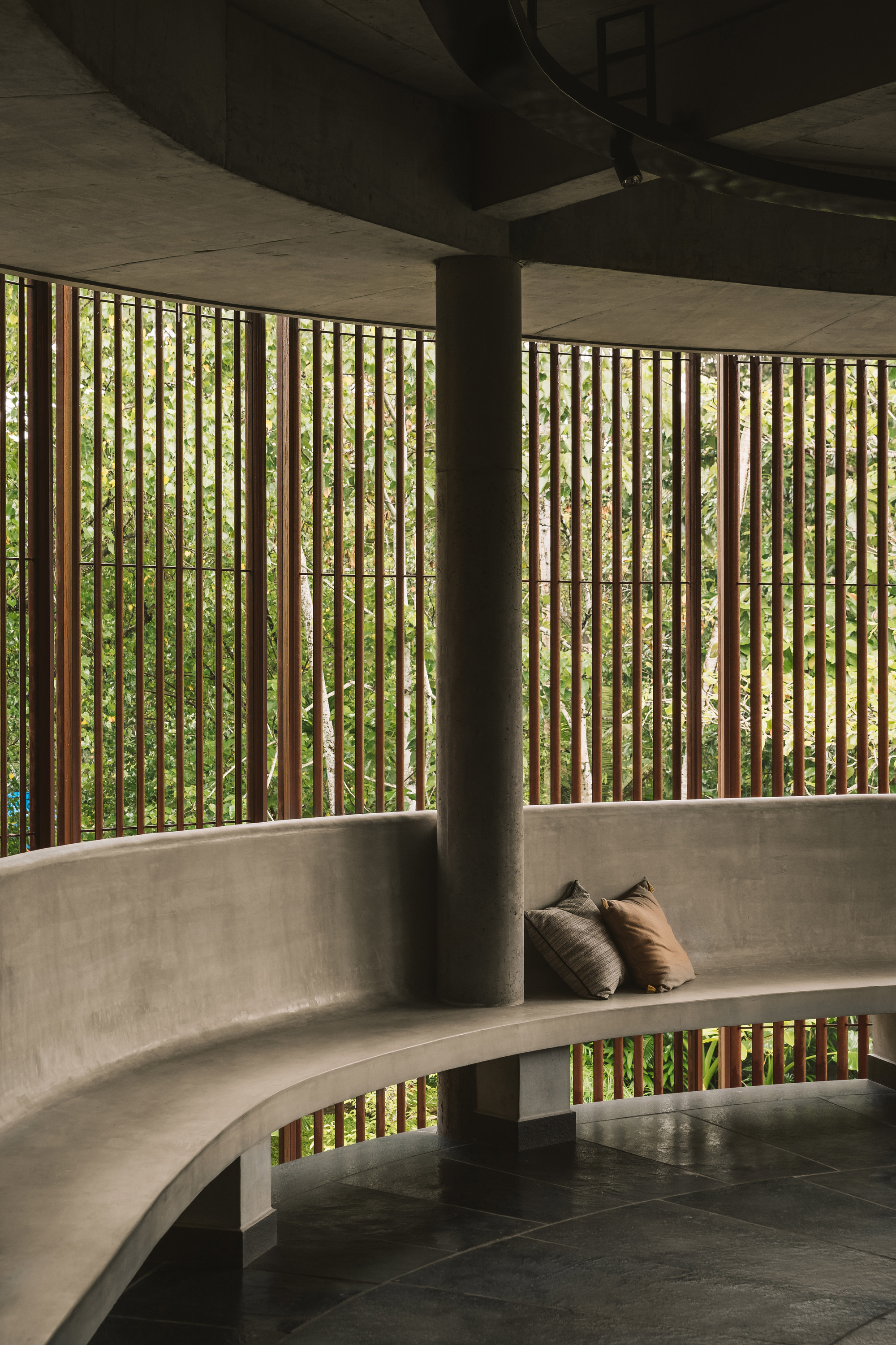 Curved concrete bench with timber screen filtering light into a shaded interior seating area