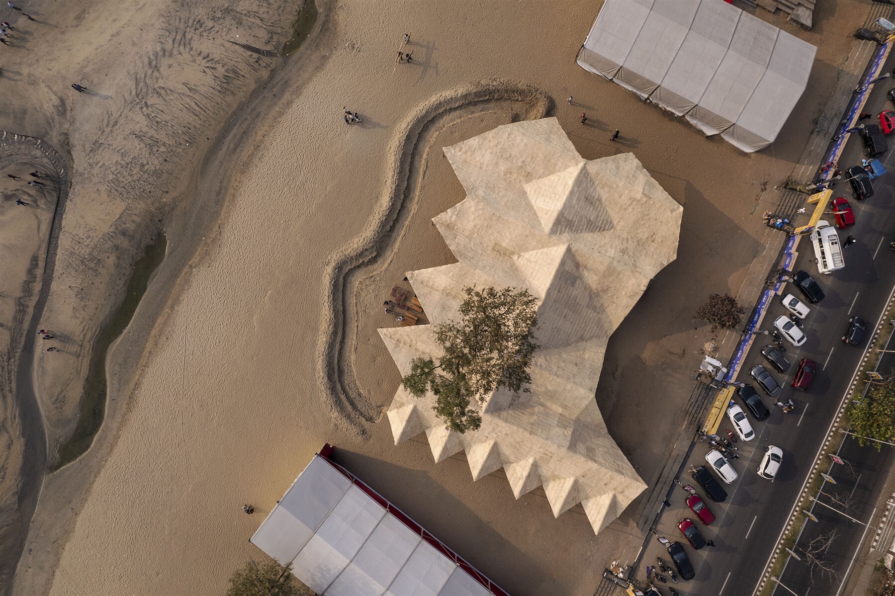 Aerial view of the zigzag woven roof surrounding a tree in a sandy compound