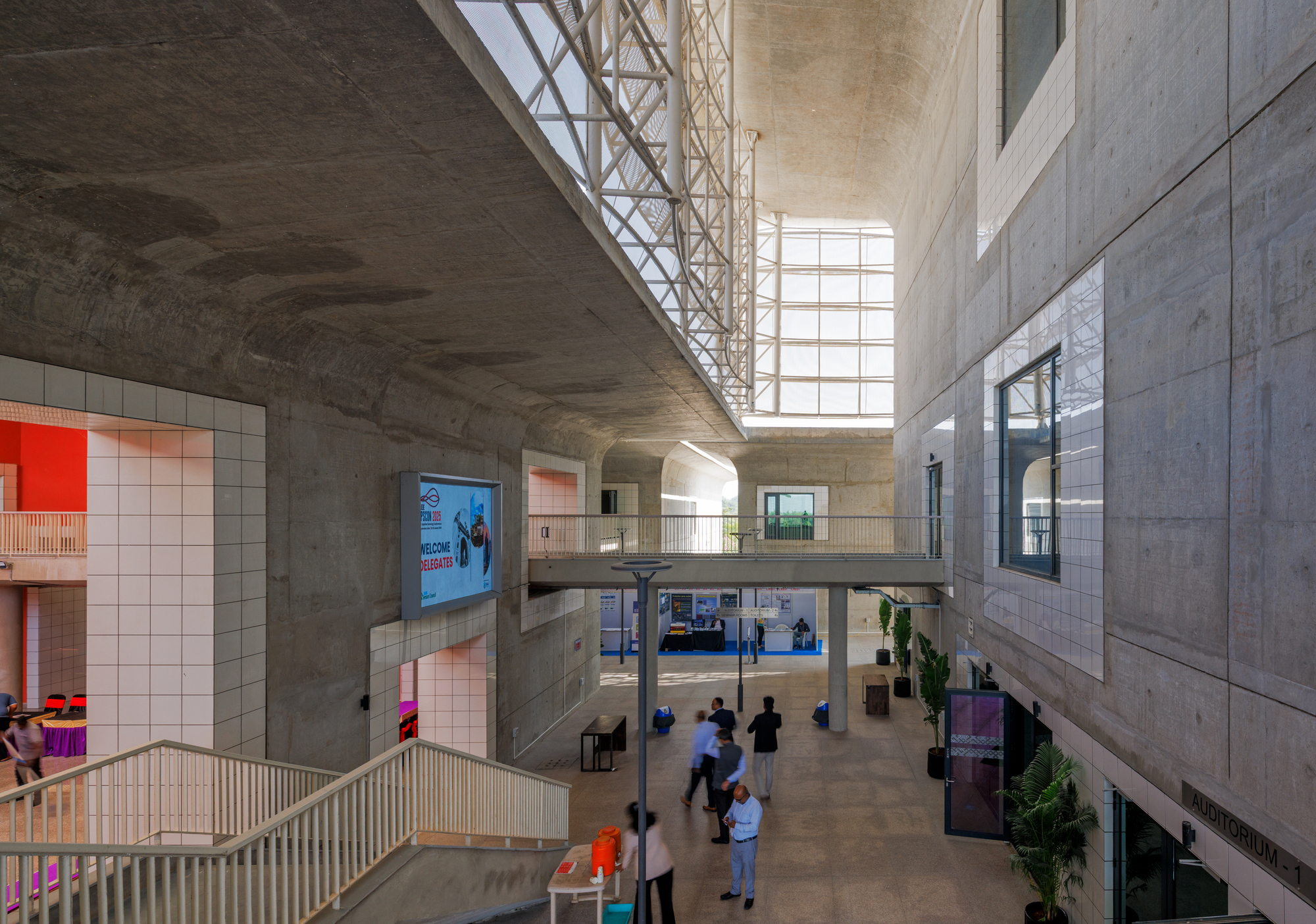 Multi-level atrium with board-formed concrete walls, tiled openings, and visitors gathered on the polished floor below