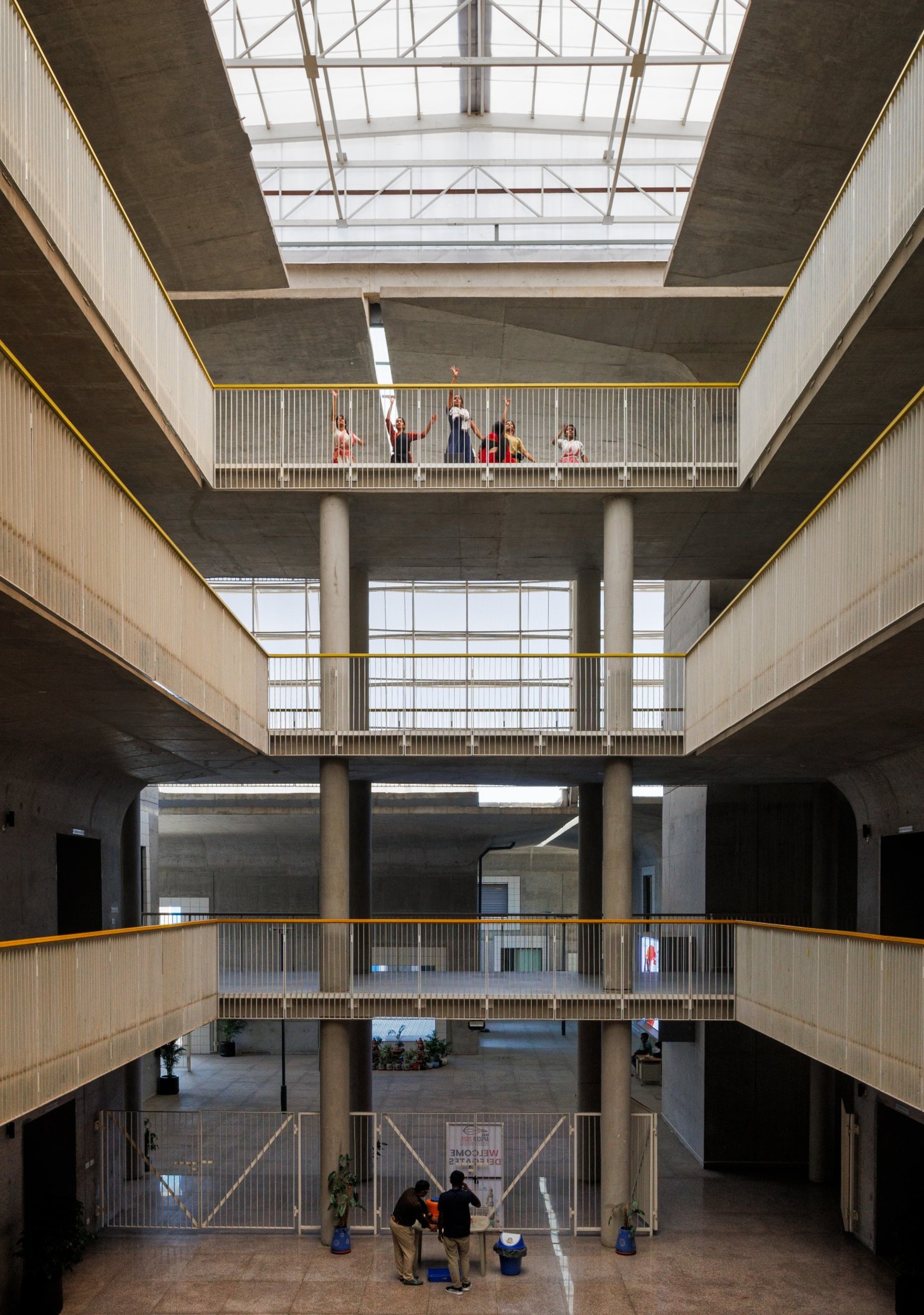 Interior courtyard with stacked concrete floors and metal railings topped by a steel truss skylight