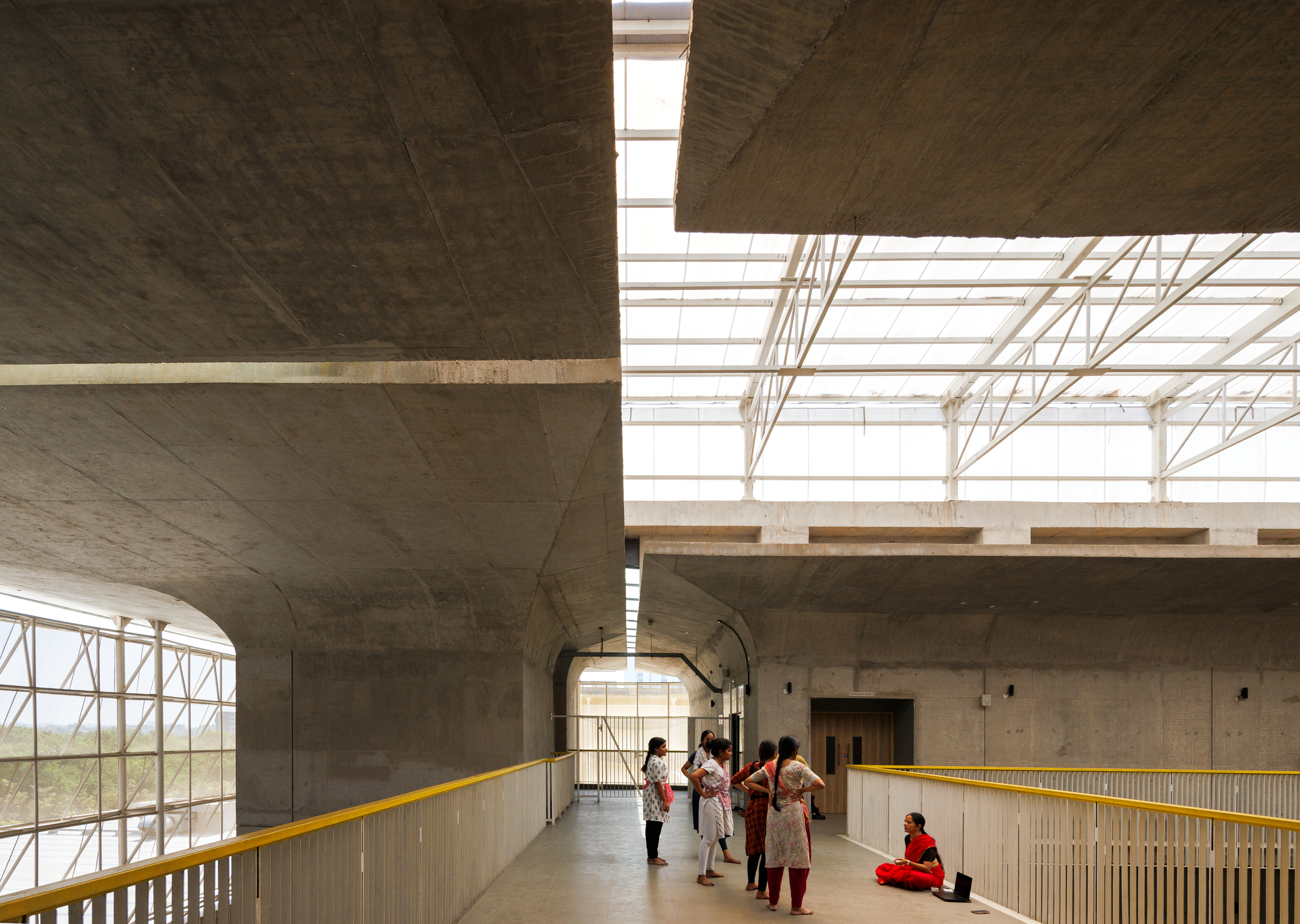 Upper level corridor with yellow metal railing overlooking the atrium under a steel truss roof