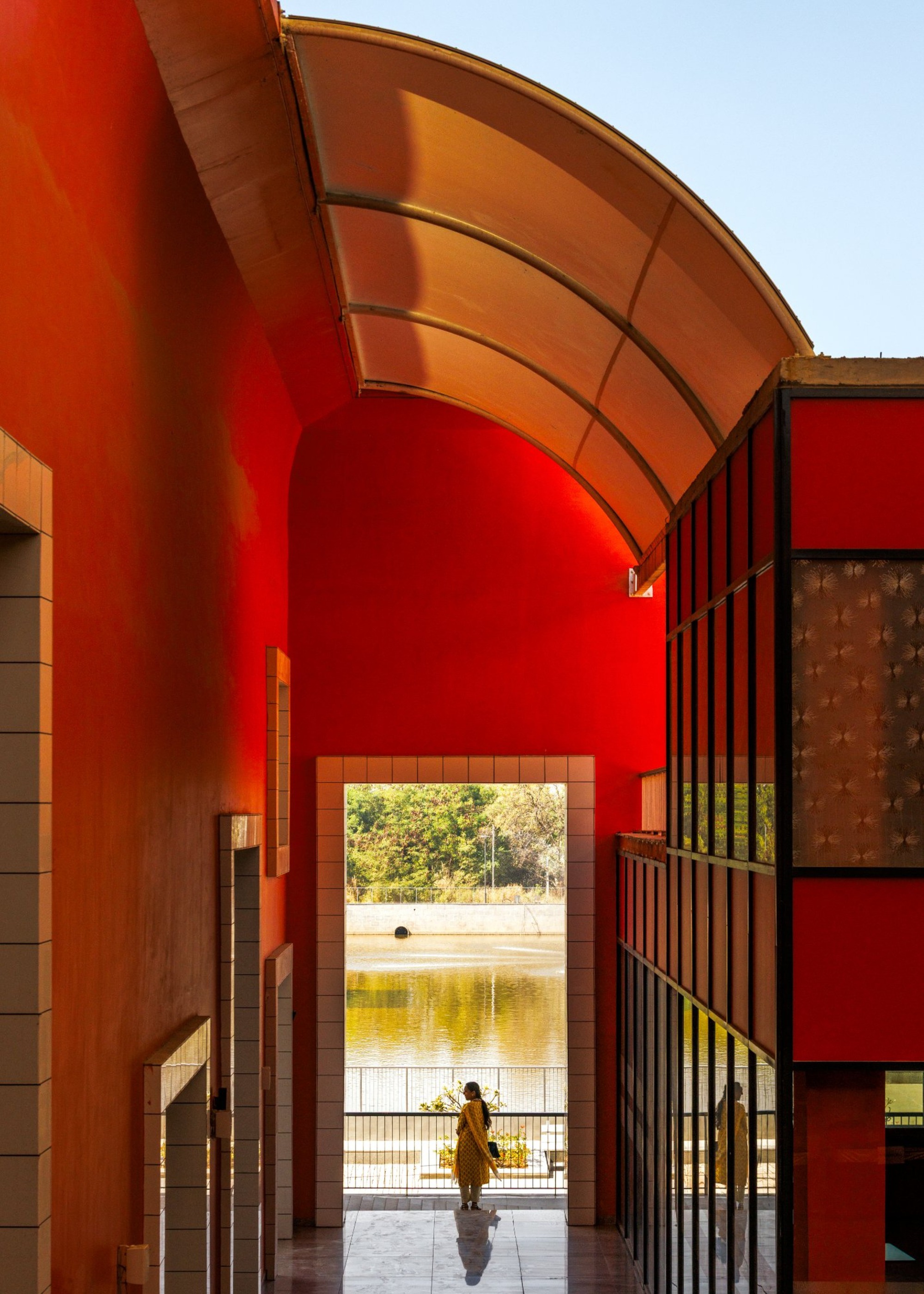 Covered walkway with curved orange metal canopy and red wall framing a view to water