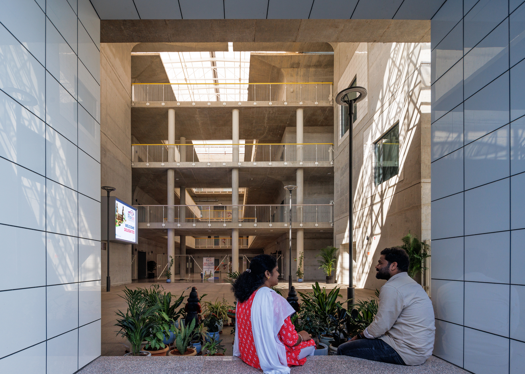 View through the central courtyard showing stacked balconies framed by white tile-clad walls with seated visitors