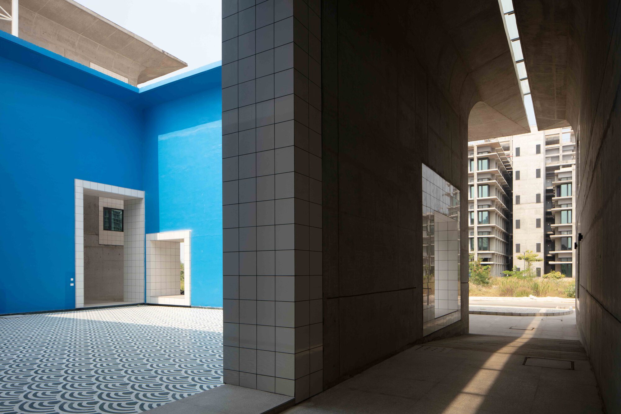 Covered walkway looking toward a blue-painted courtyard framed by white tile columns and concrete ceiling slot