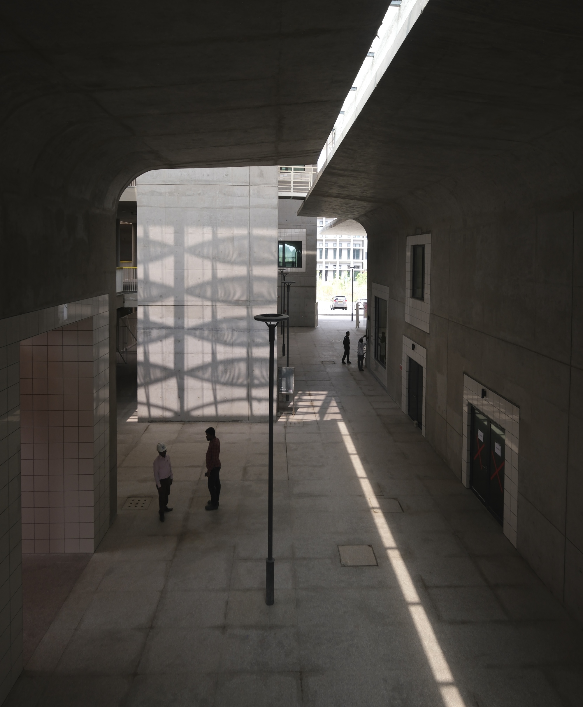 Interior street with translucent screen wall and shaft of sunlight casting shadows on concrete pavement