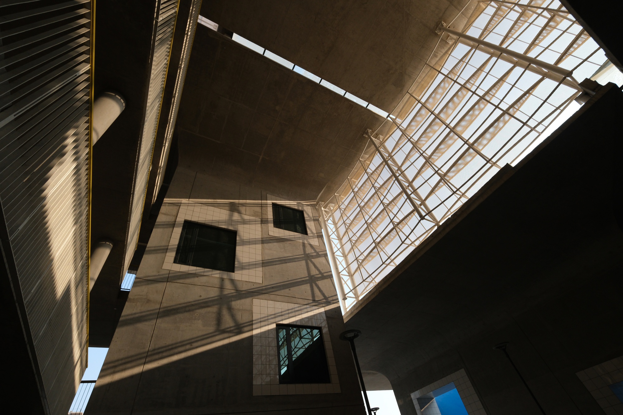 Upward view of the central atrium with gridded skylight and concrete balconies in bright daylight