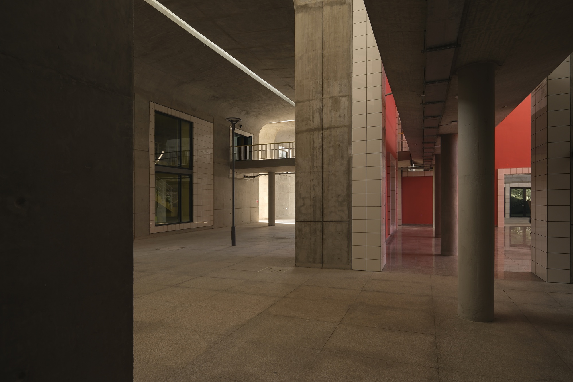 Ground floor corridor with exposed concrete columns and ceiling and red-lit passage at dusk