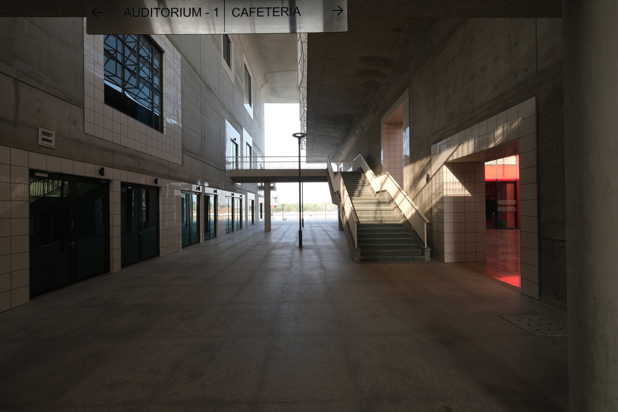 Interior lobby with central staircase and directional signage under concrete vaults with afternoon light