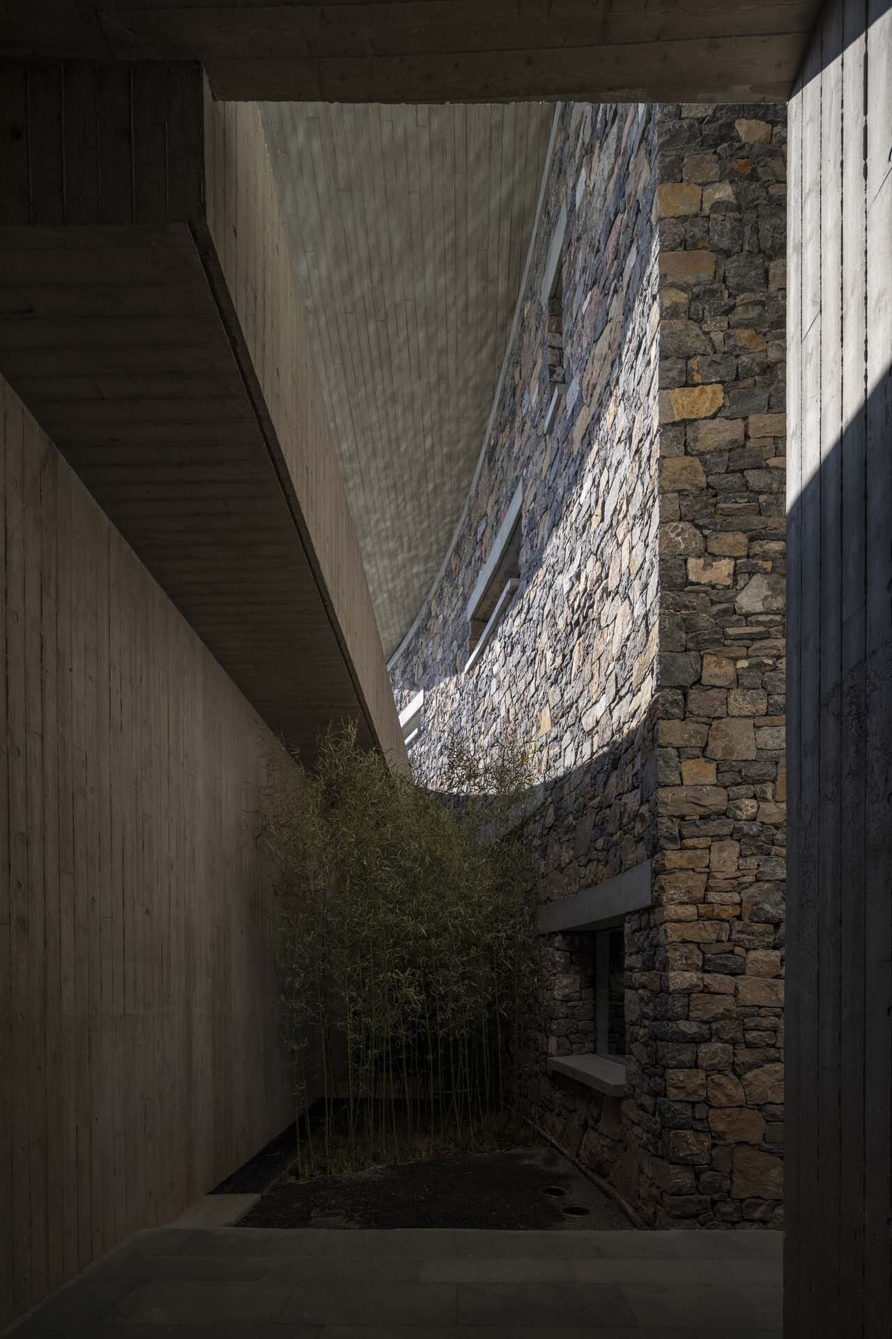 Courtyard view looking up through a curved opening in the stone wall with bamboo below