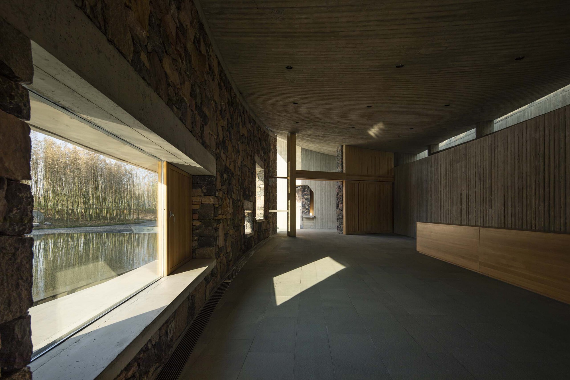 Corridor with stone wall and horizontal window overlooking a pond and birch trees in autumn
