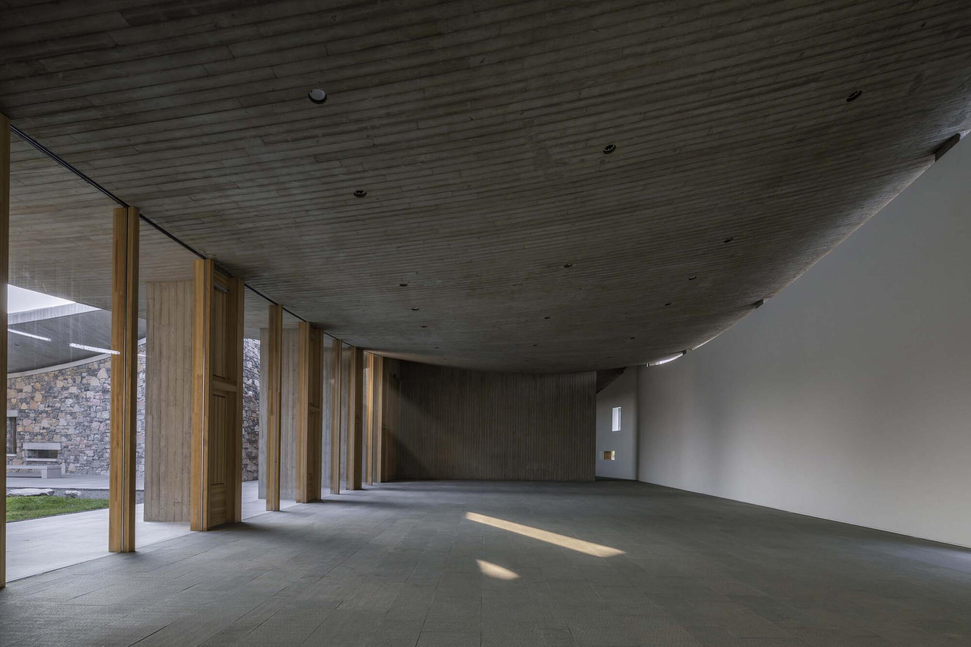 Gallery space with angled timber ceiling and timber columns opening to a courtyard