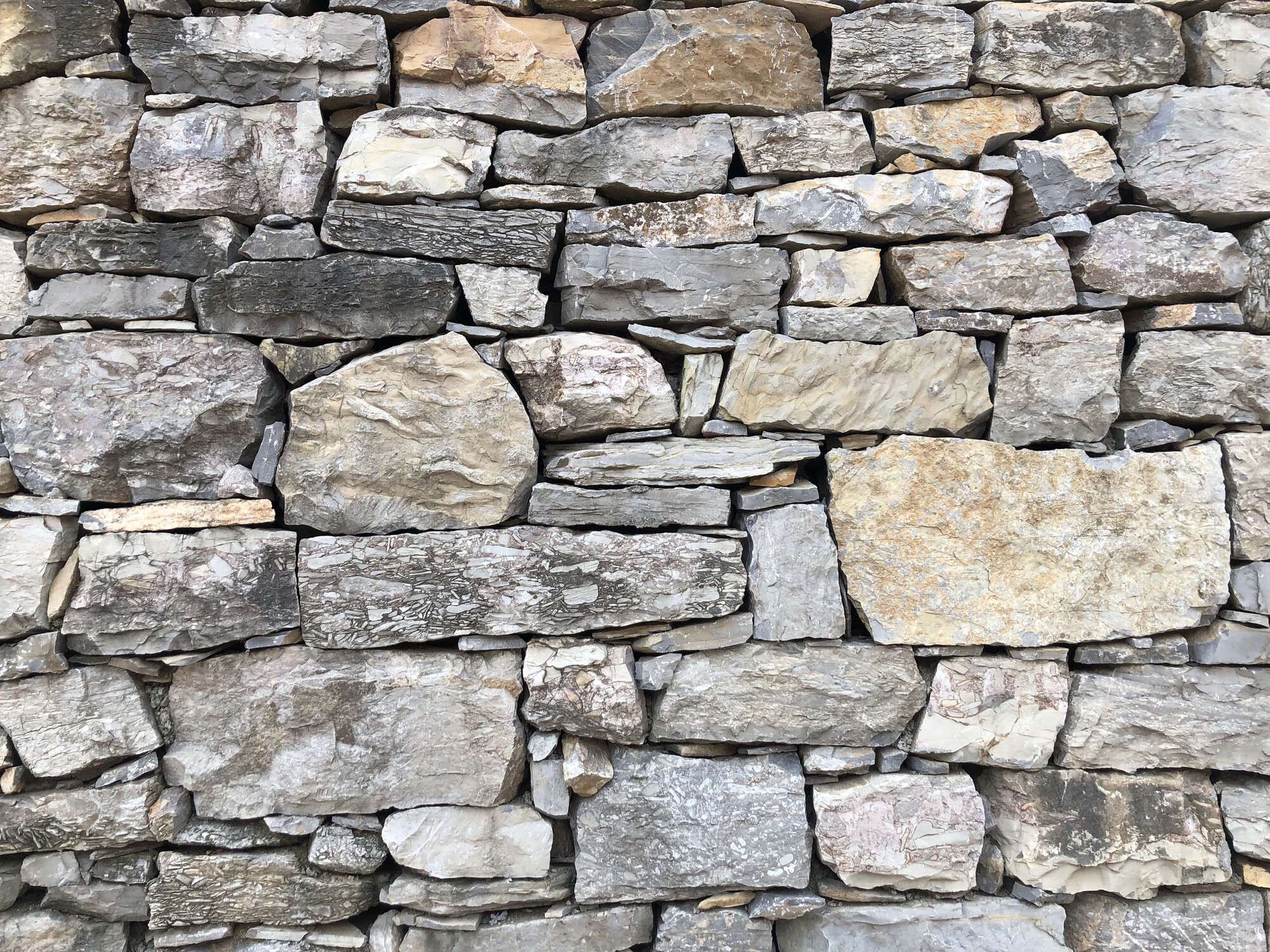 Dry-stacked fieldstone wall in grey and tan tones with varied coursing and natural patina