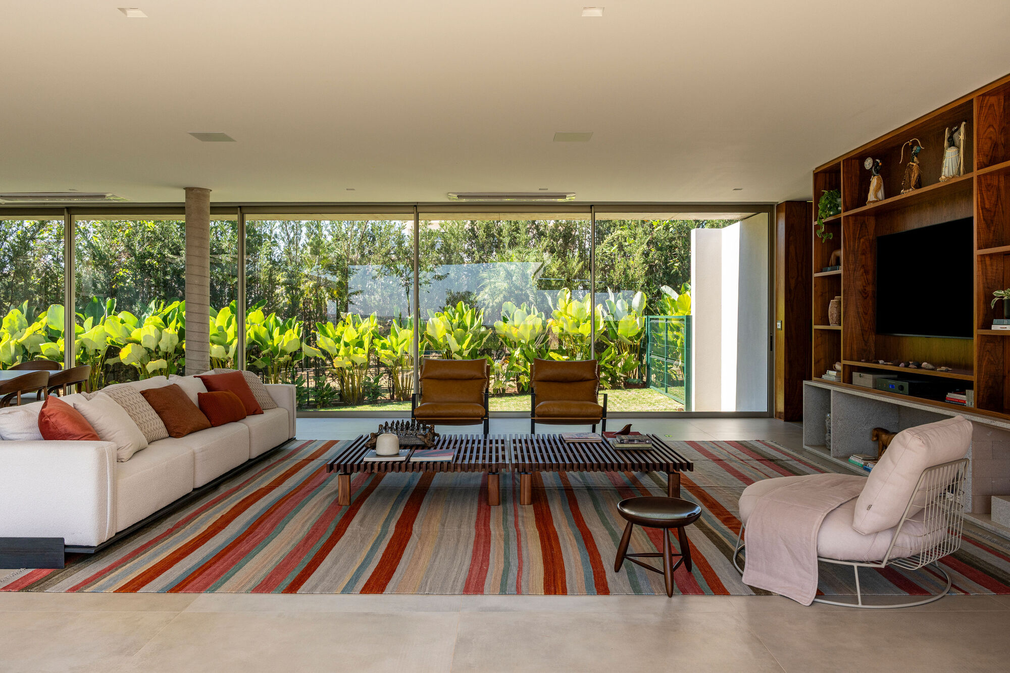 Living room with striped rug and floor-to-ceiling glazing opening to a terrace with banana plants